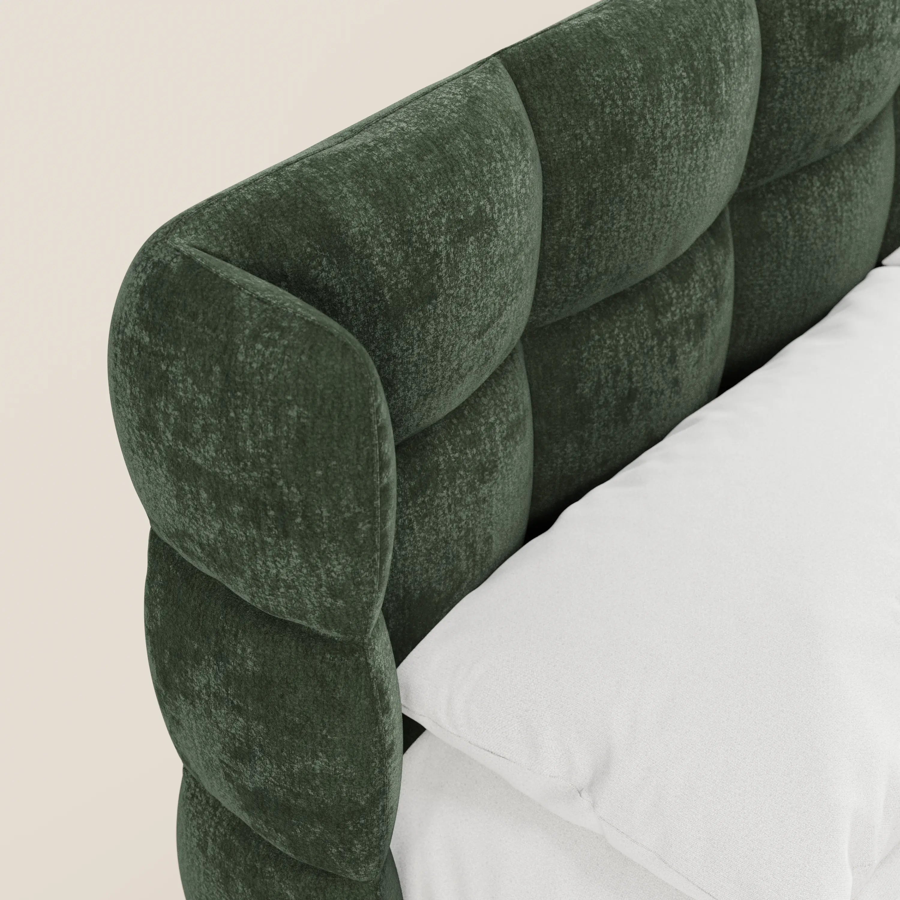 Primo piano del letto imbottito RAGNAR di Letti.store, con una morbida testiera avvolgente capitonné di colore verde scuro, realizzata in tessuto certificato Oeko-Tex®. I cuscini e la biancheria da letto bianchi risaltano sullo sfondo beige chiaro.