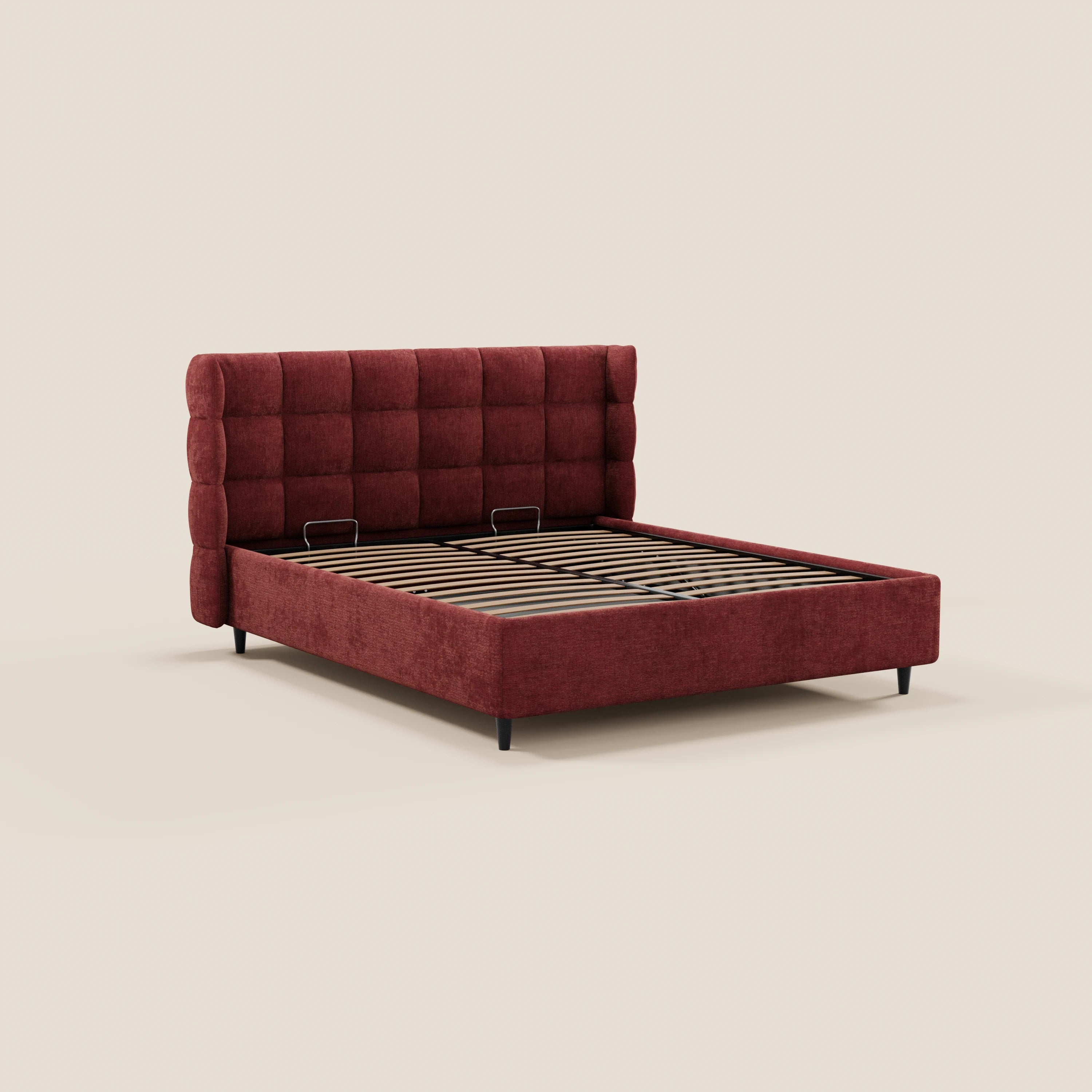 Il letto imbottito RAGNAR di Letti.store presenta una testiera avvolgente capitonné in tessuto rosso intenso certificato Oeko-Tex®, una base a doghe in legno con vano contenitore, gambe corte nere ed è messo in risalto da uno sfondo chiaro a tinta unita.