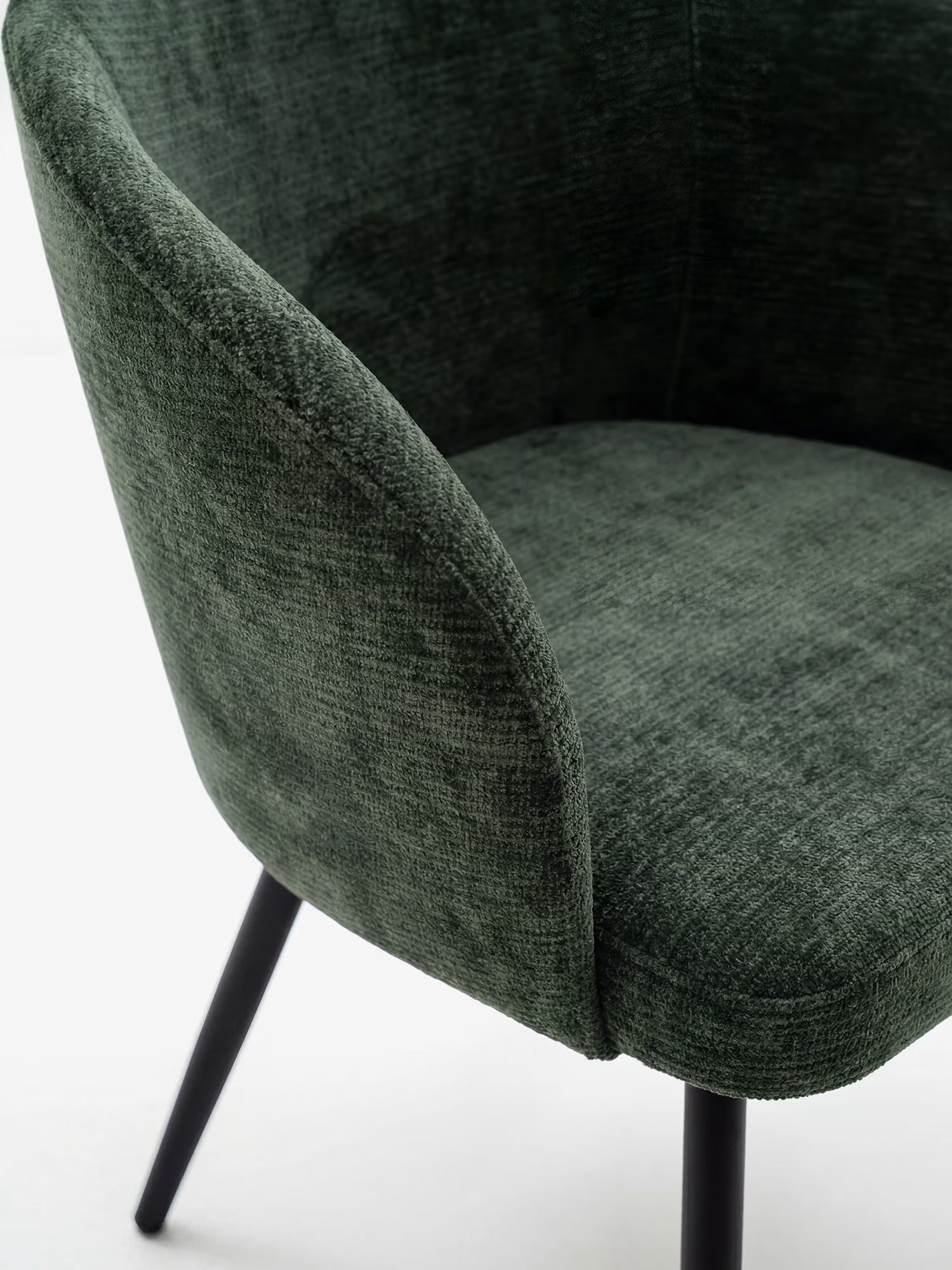 Un primo piano della sedia Rovo con braccioli di Divani.Store, caratterizzata da un morbido rivestimento in ciniglia verde scuro, uno schienale ricurvo e sottili gambe in metallo nero. Il design morbido e moderno risalta sullo sfondo bianco a tinta unita.