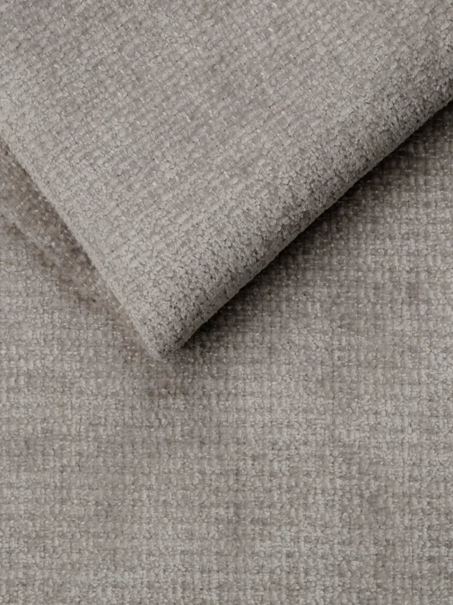 Un primo piano del tessuto intrecciato grigio chiaro e dalla trama ruvida che riveste il divano letto Ottaviano con letto estraibile – penisola reversibile e contenitore in tessuto materico lavabile, che mostra un motivo morbido e finemente granuloso nei punti in cui il tessuto è piegato.
