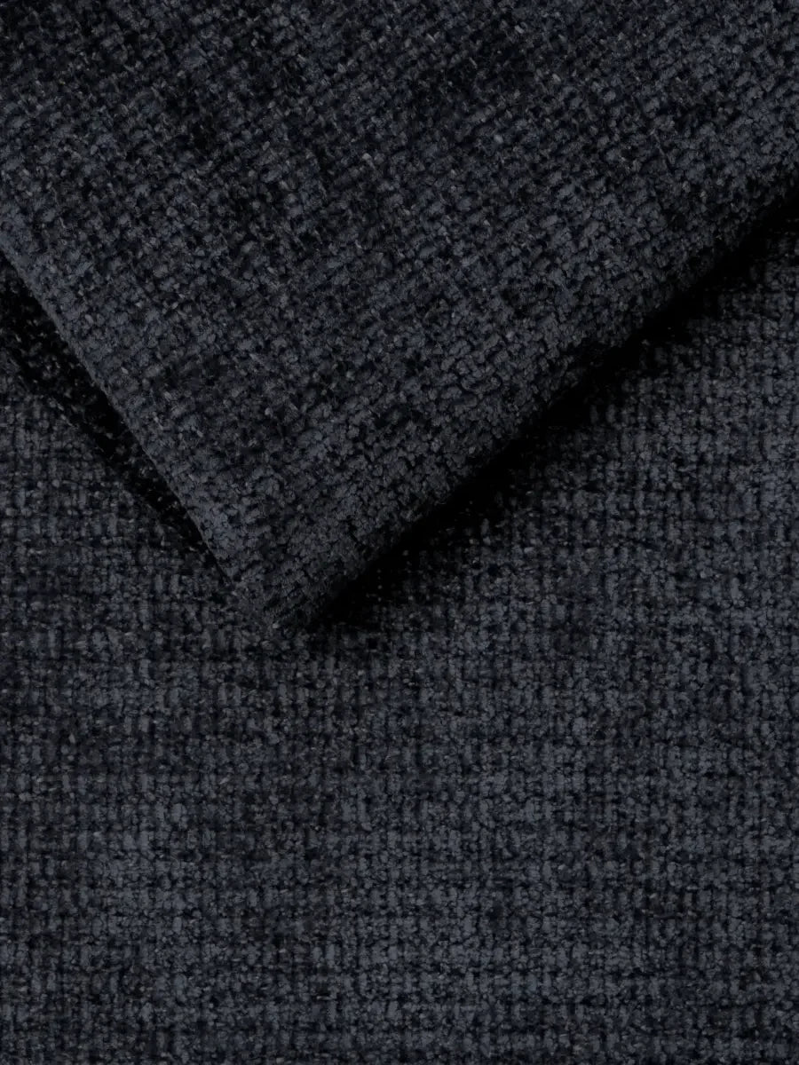 Un primo piano di un tessuto grigio antracite scuro dalla trama spessa e irregolare, ripreso piegato in un angolo per mettere in risalto la trama del divano letto Ottaviano con letto estraibile - penisola reversibile e contenitore in tessuto materico lavabile.