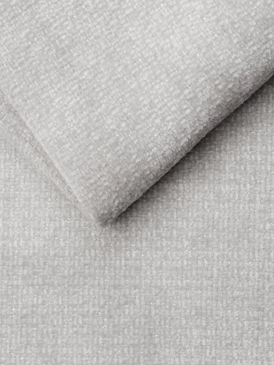 Un primo piano del tessuto intrecciato grigio chiaro e dalla trama ruvida che riveste un divano letto Ottaviano con letto estraibile – penisola reversibile e contenitore in tessuto materico lavabile, ripreso da chiuso per evidenziarne la superficie morbida e piacevole al tatto.