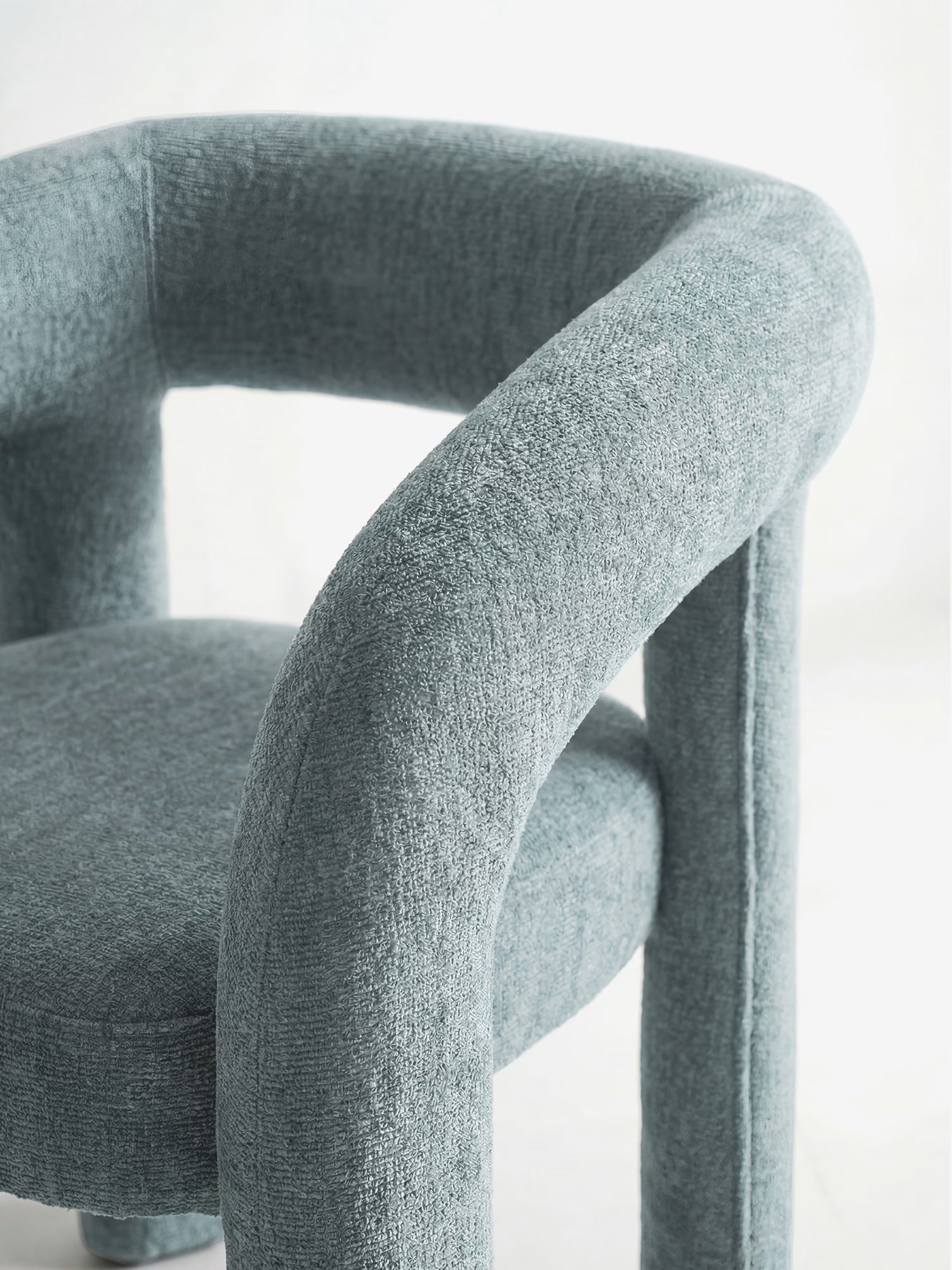 Un primo piano della sedia di design Sibilla, interamente imbottita in tessuto, di Divani.Store, caratterizzata da un rivestimento grigio-azzurro, uno schienale imbottito ad arco e gambe cilindriche: perfetta per dare un tocco di design contemporaneo.