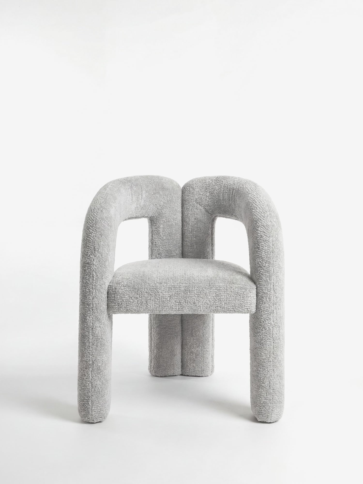 La Sibilla di Divani.Store è una sedia dal design contemporaneo, imbottita e rivestita in tessuto grigio, con una struttura ad arco che unisce le gambe e i braccioli in uno schienale parziale, su sfondo bianco.