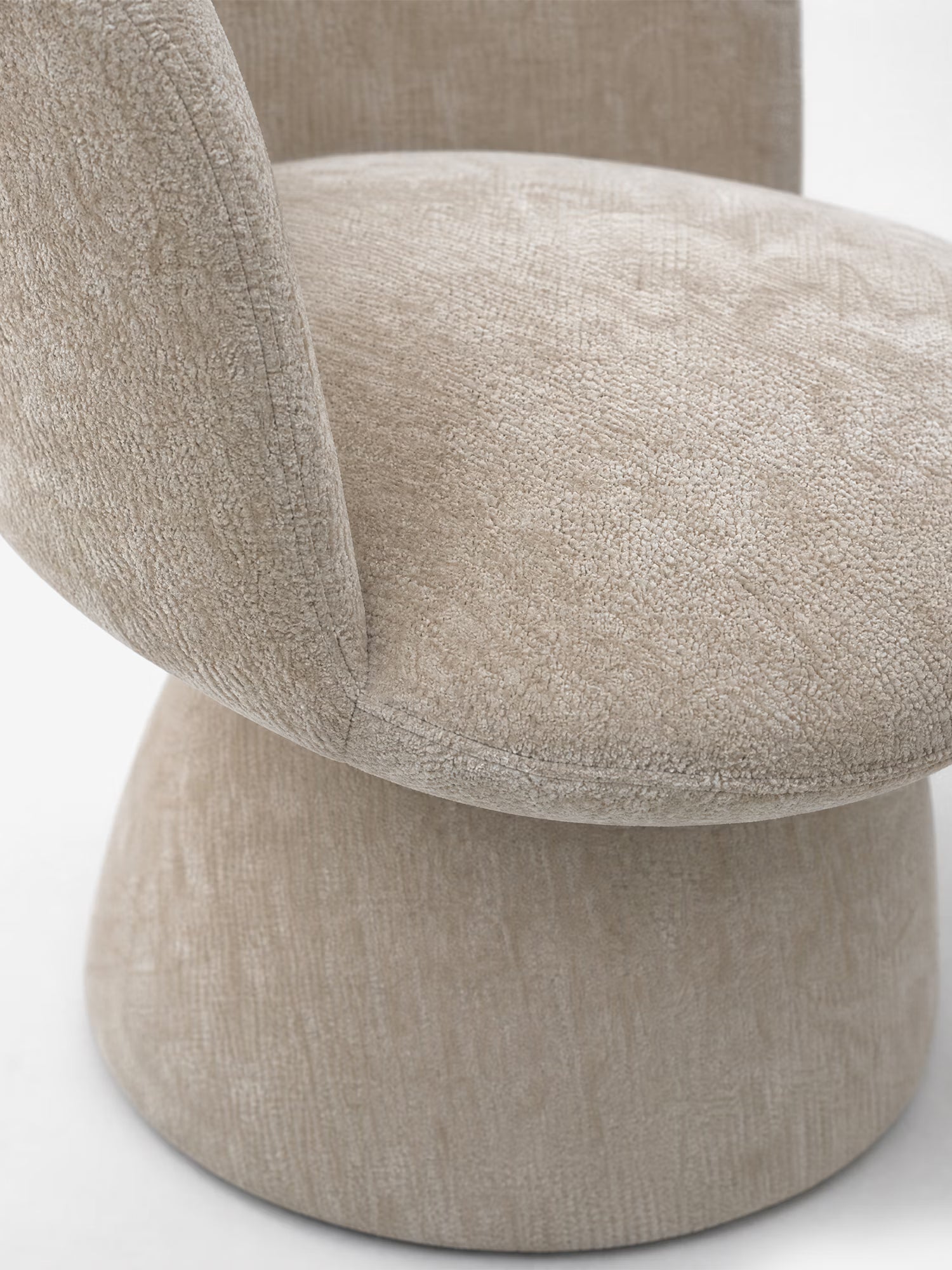 Primo piano della sedia moderna imbottita Talia di Divani.Store, realizzata in morbido tessuto ciniglia beige certificato OEKO-TEX® e caratterizzata da un'ampia base cilindrica. Lo sfondo bianco mette in risalto le eleganti curve della sedia e il suo raffinato rivestimento.