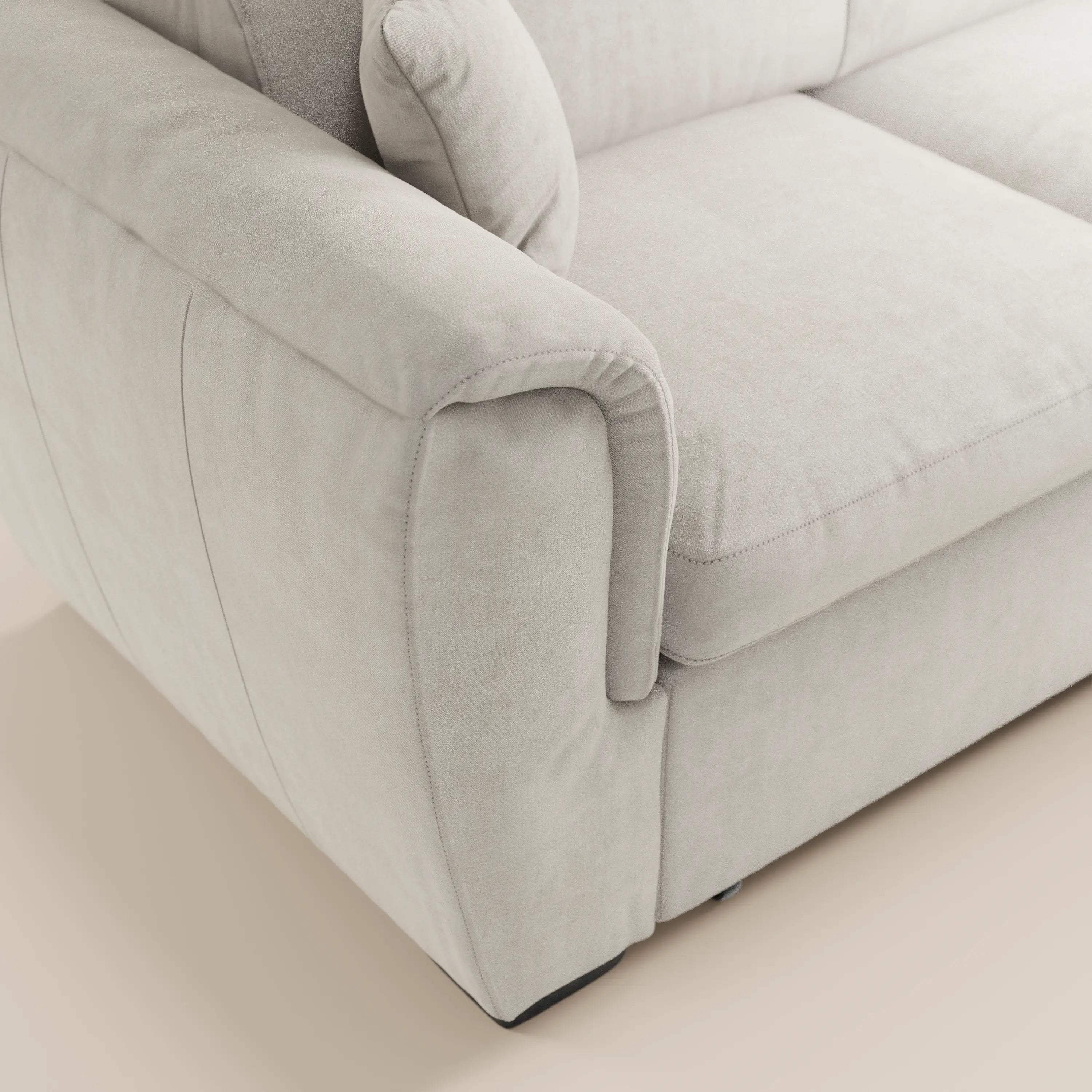 Primo piano del divano angolare reversibile Titano di Divani.Store in tessuto beige chiaro, smacchiabile e certificato Oeko-Tex®; imbottitura morbida con ampi braccioli, schienale, cuscino coordinato e cuciture a vista su un pavimento neutro.