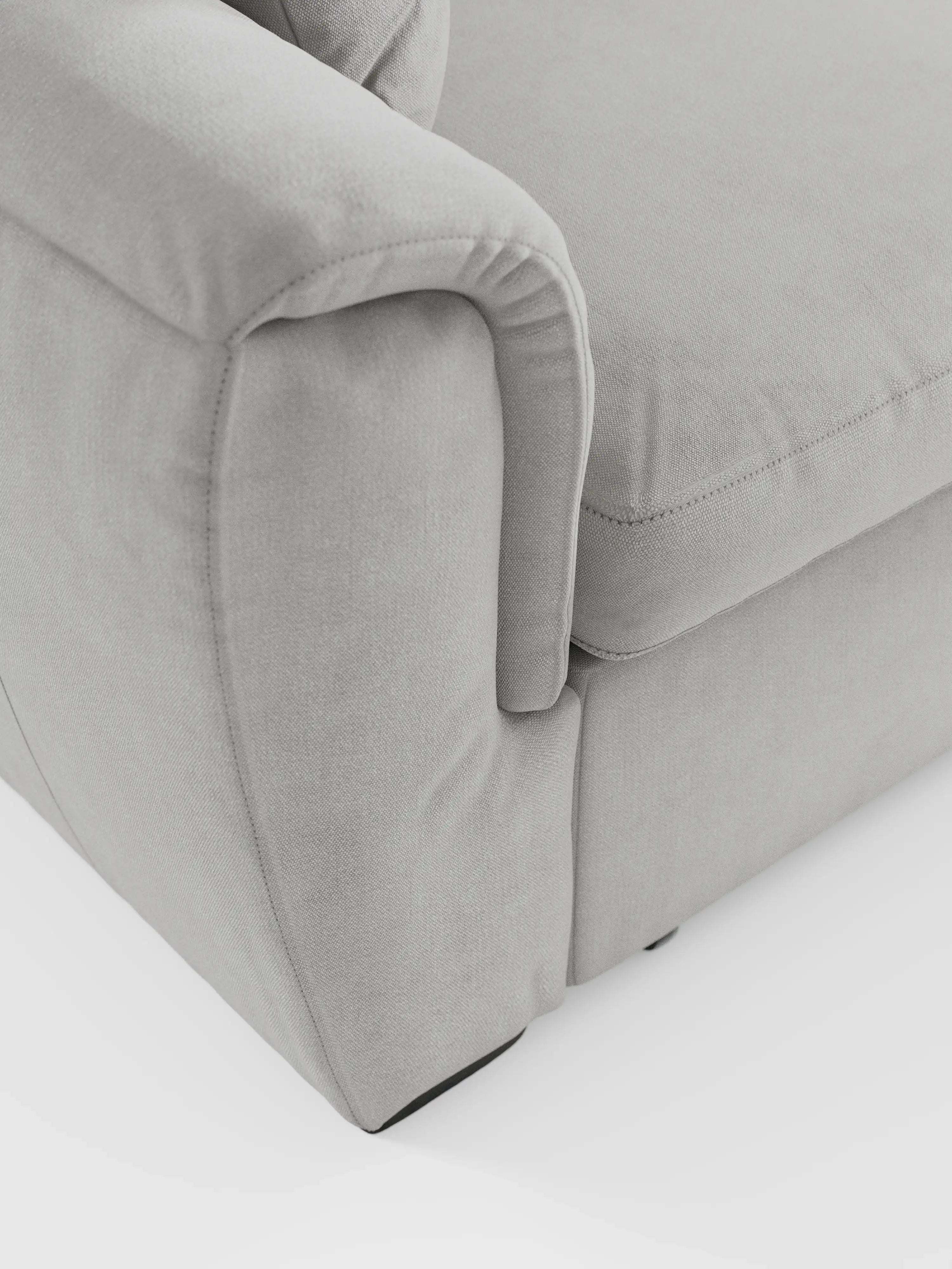 Primo piano del divano angolare reversibile con contenitore estraibile e pouf Titano, di colore grigio chiaro, di Divani.Store, con i cuscini dei braccioli e della seduta. Il tessuto Oeko-Tex®, liscio e facile da pulire, presenta sottili dettagli di cucitura e una trama raffinata su uno sfondo bianco a tinta unita. Questa immagine mette in risalto il design morbido e arrotondato e i contorni delicati di questo divano versatile dotato di poggiatesta regolabili.