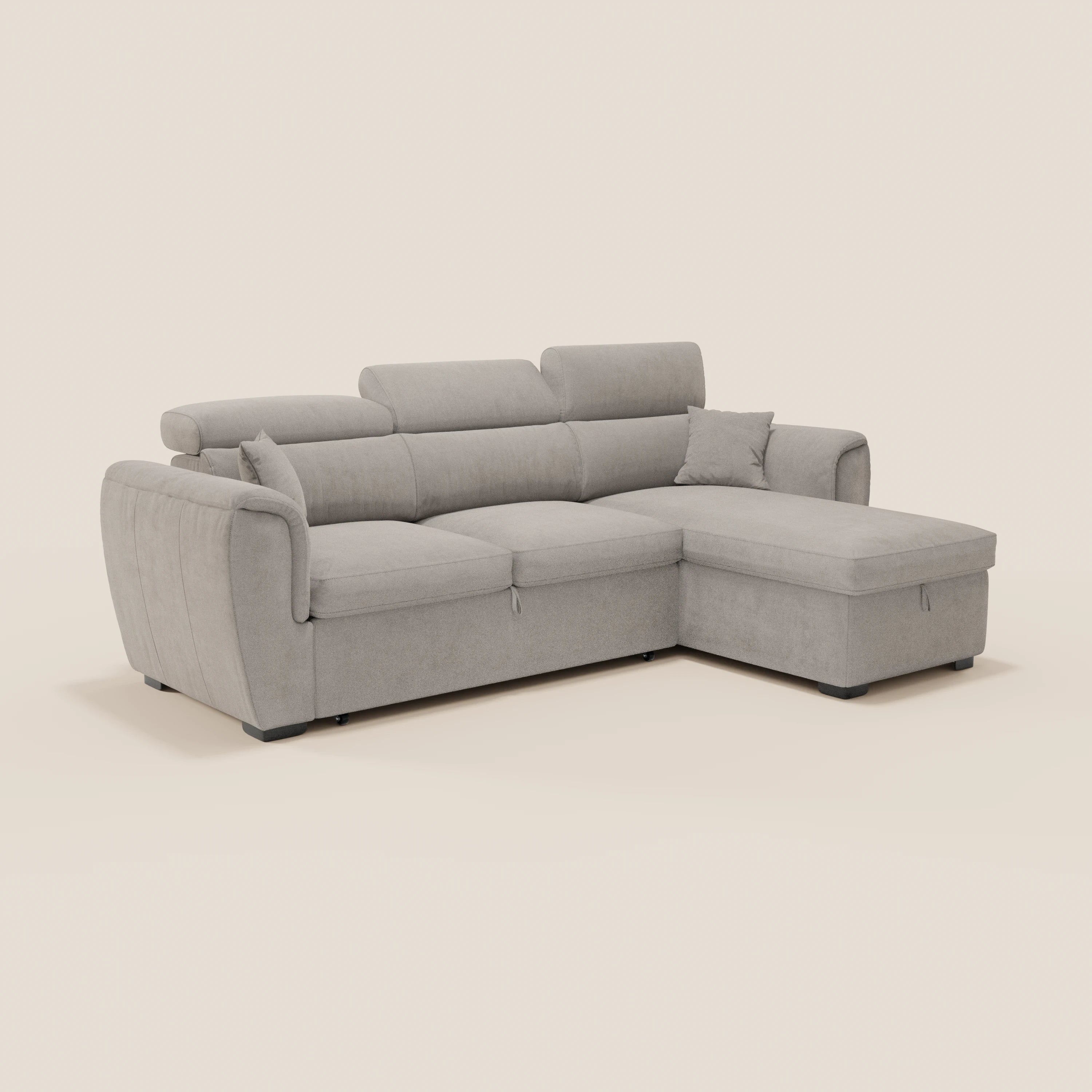 Il divano letto Titano di Divani.Store è dotato di una chaise longue reversibile con vano portaoggetti, poggiatesta reclinabili, elemento estraibile e tessuto antimacchia. Nella foto è raffigurato in grigio chiaro con morbidi cuscini e gambe basse nere su uno sfondo bianco sporco.