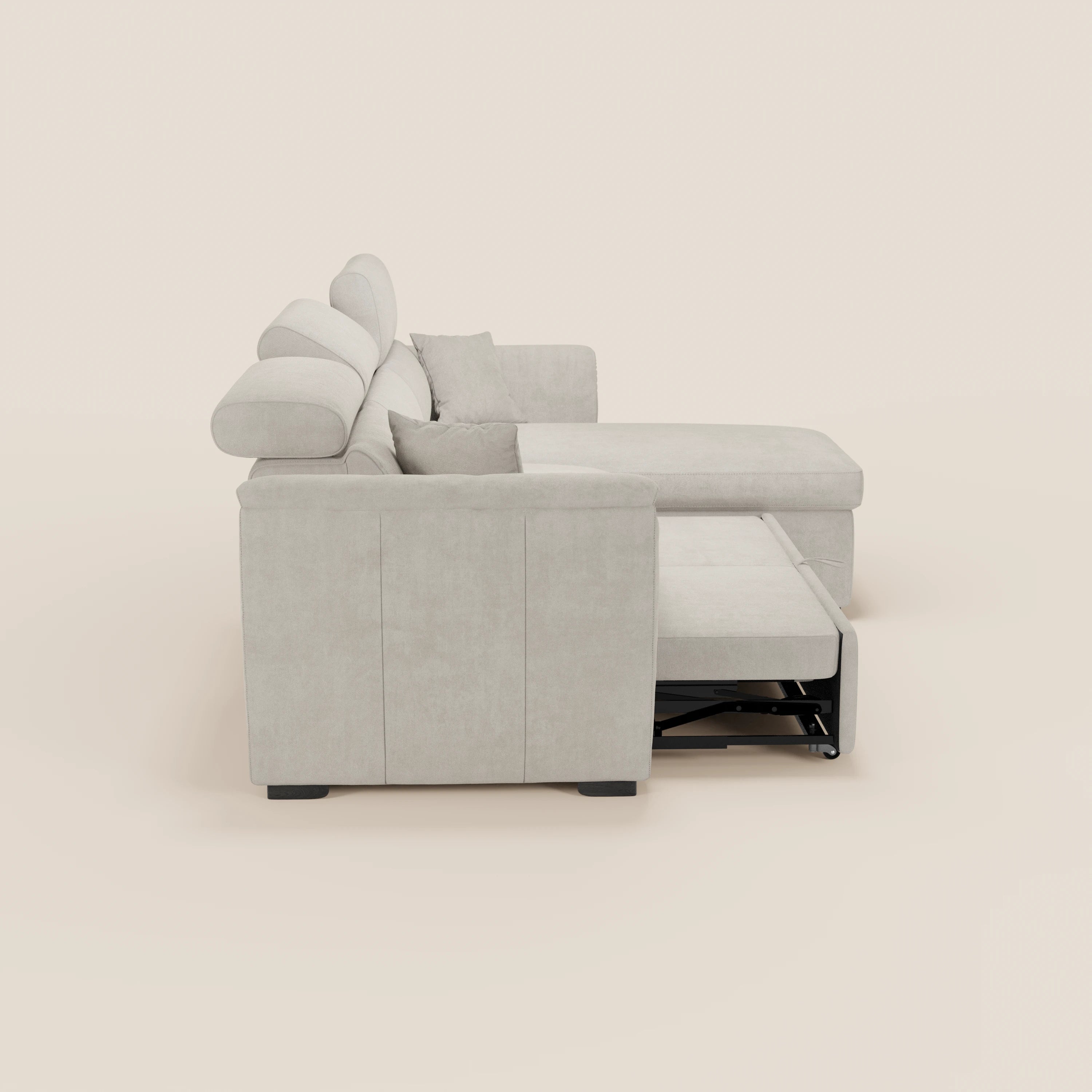 Il divano letto Titano di Divani.Store, qui raffigurato di profilo in tessuto beige chiaro, è dotato di una chaise longue reversibile con vano portaoggetti, poggiatesta regolabili, due cuscini coordinati e un letto estraibile. Lo sfondo è semplice e neutro.