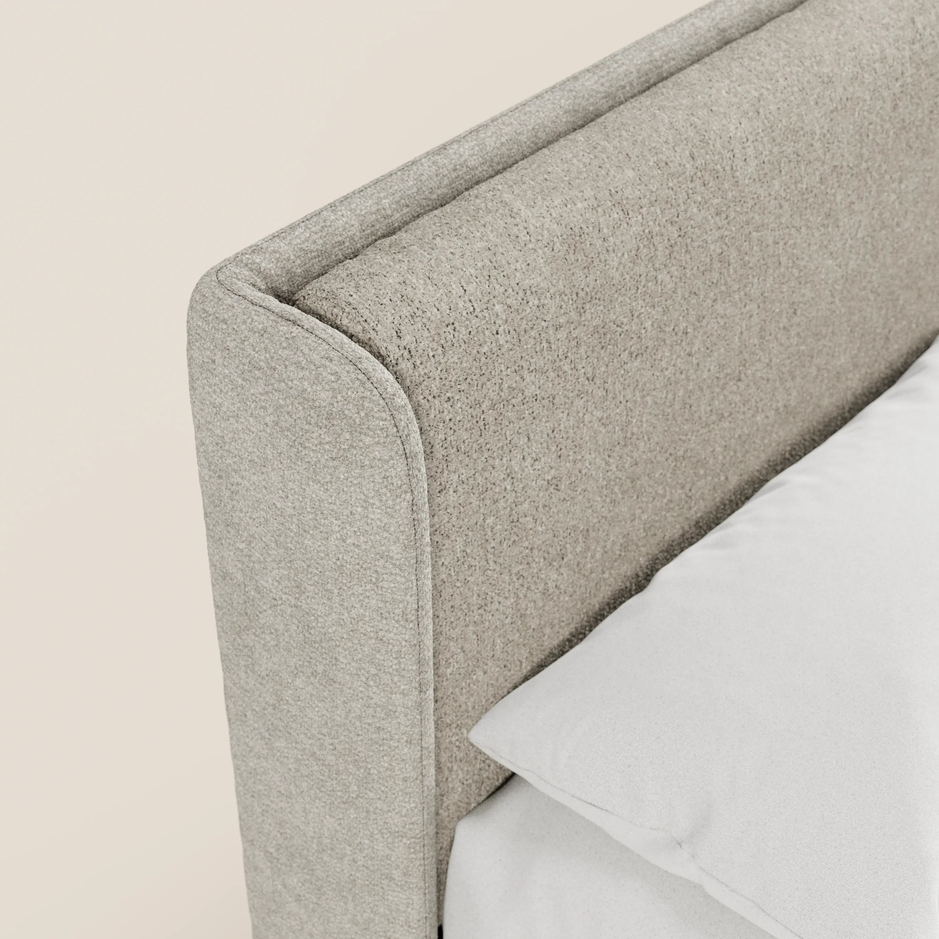 Primo piano del letto imbottito bicolore VALKIRIA di Letti.store, caratterizzato da una base contenitiva, una testiera avvolgente dalle linee curve e cuscini schienali. La biancheria da letto bianca crea un contrasto con il moderno design italiano su uno sfondo neutro chiaro.