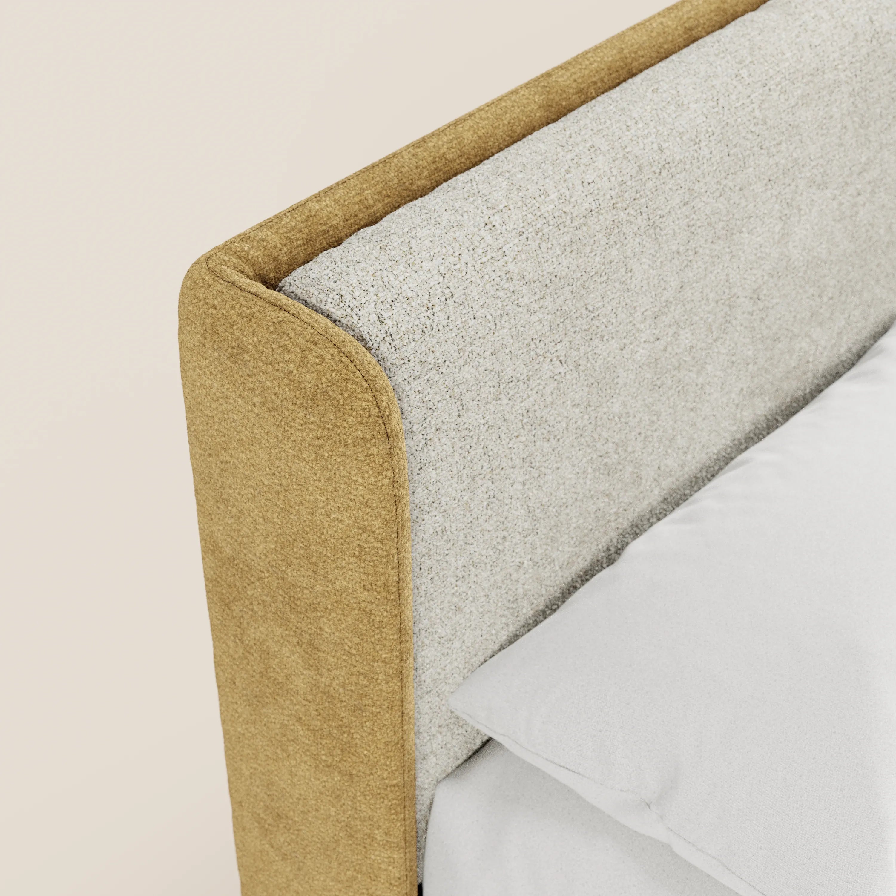 Primo piano del letto imbottito bicolore VALKIRIA di Letti.store, caratterizzato da una testiera curva e avvolgente rivestita con tessuto beige chiaro a trama e tessuto liscio giallo senape. Sul letto sono appoggiati un cuscino bianco e un lenzuolo, su uno sfondo chiaro e uniforme.