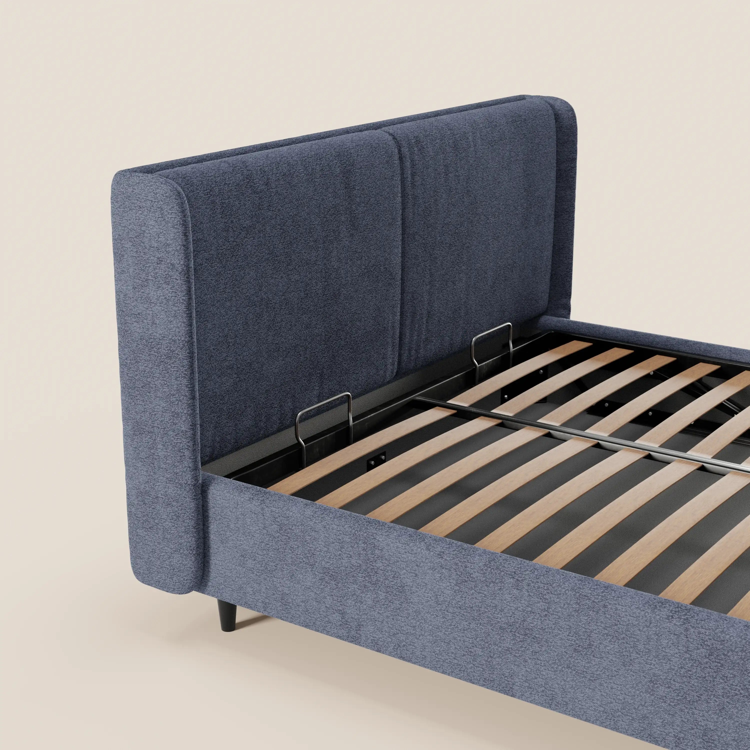 Un primo piano del letto di design VALKIRIA di Letti.store mette in risalto la sua testiera avvolgente con 2 cuscini imbottiti e tessuto Oeko-Tex®. Le doghe in legno, la struttura in metallo nero e le corte gambe nere risaltano sullo sfondo beige chiaro.