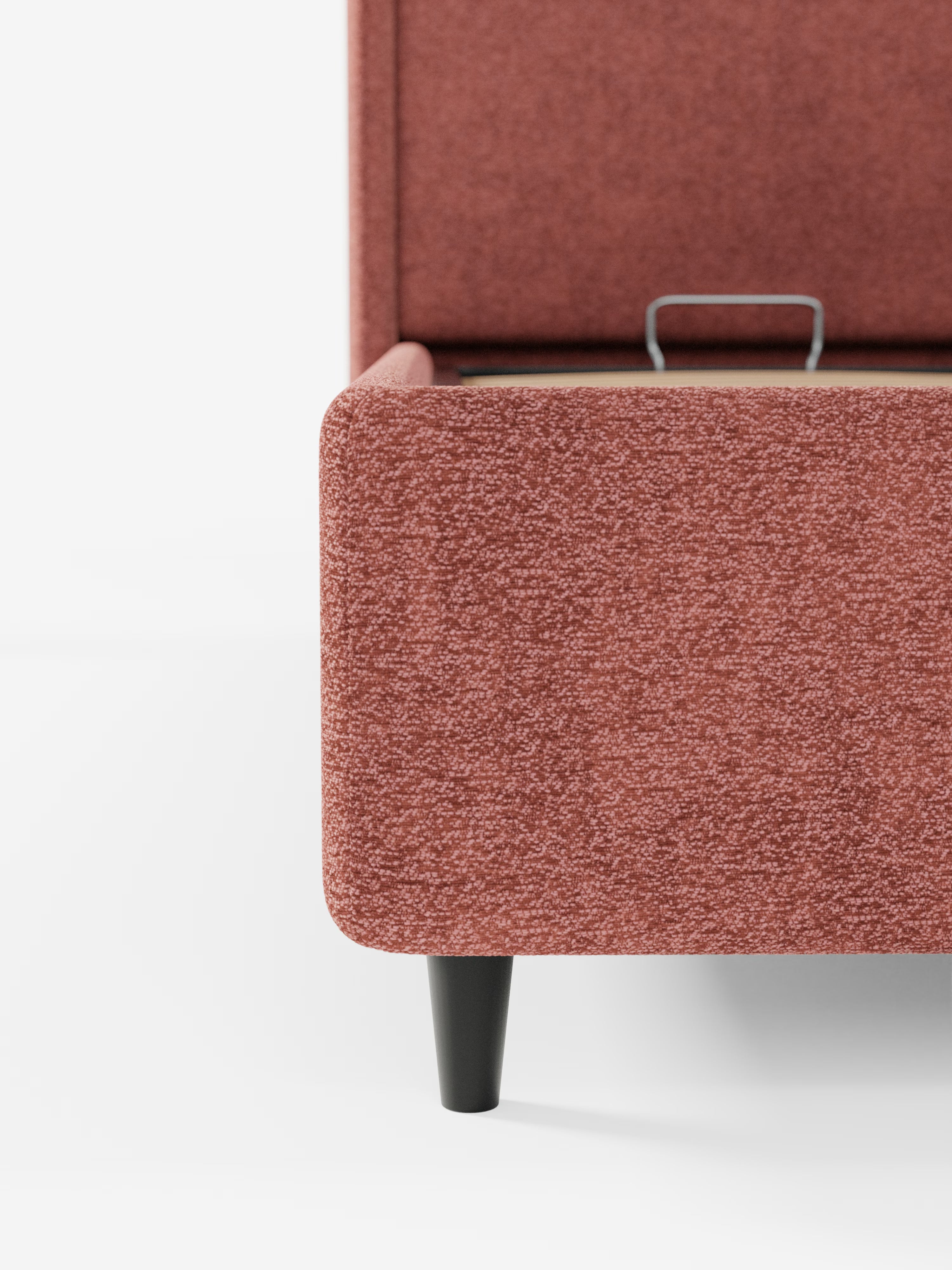Primo piano del letto di design VALKIRIA con vano contenitore e testiera avvolgente di Letti.store, un letto rettangolare imbottito di colore rosa con gambe affusolate nere. L’angolo visibile ne sottolinea il raffinato design contemporaneo, mentre una leggera fessura nella parte superiore ne suggerisce la funzione pratica di letto contenitore. Sullo sfondo bianco a tinta unita, risaltano la trama e il colore del tessuto certificato Oeko-Tex® e dei due cuscini imbottiti.