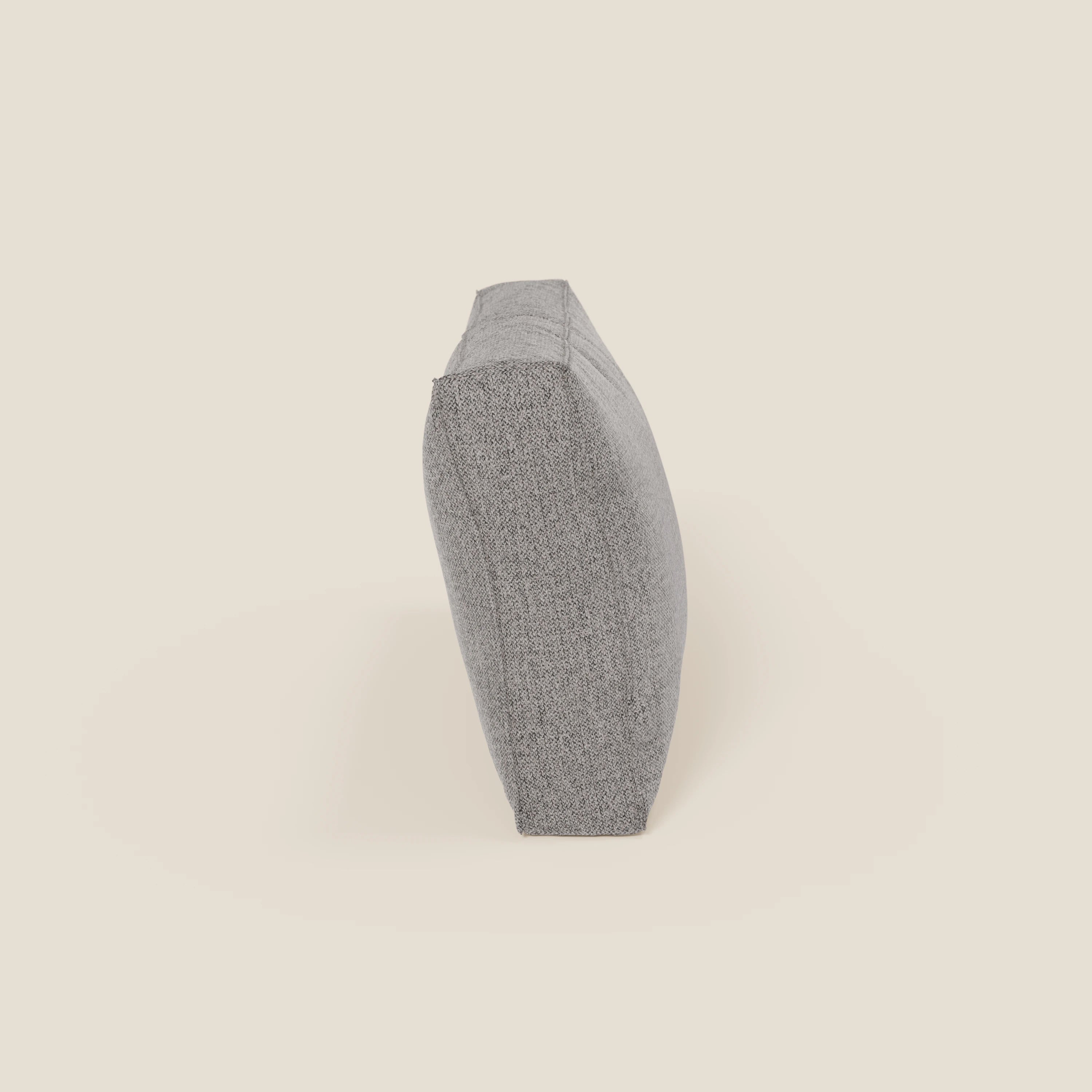Un cuscino schienale rettangolare BonBon in tessuto smacchiabile T23 grigio di Divani.Store si erge su un lato su uno sfondo bianco sporco, con una finitura sottilmente strutturata, spigoli vivi e una leggera cucitura.