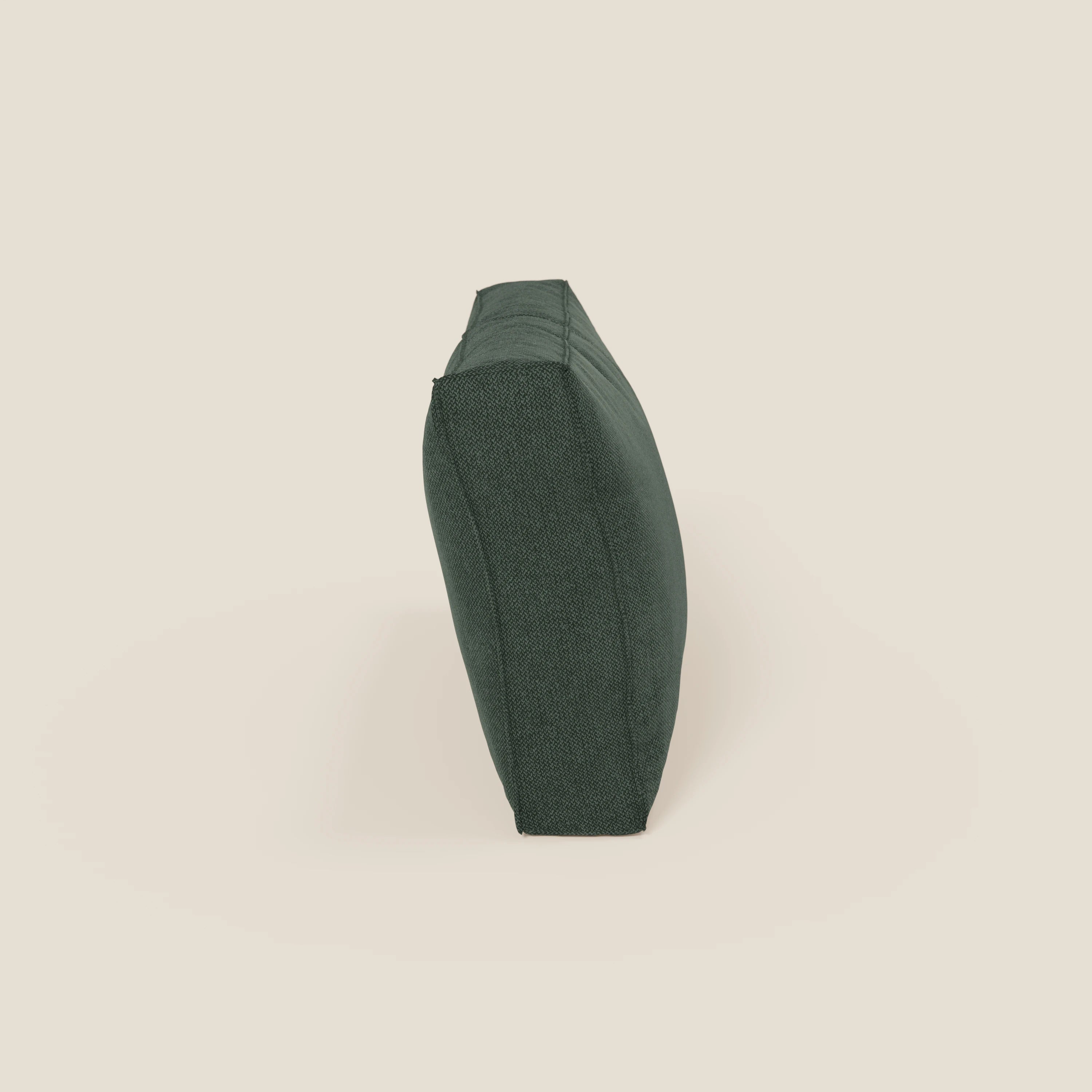 Il cuscino schienale BonBon di Divani.Store, presentato in tessuto smacchiabile T23 verde, si erge sul bordo su uno sfondo beige chiaro, mettendo in evidenza il colore verde scuro, la forma rettangolare e le cuciture laterali a vista.