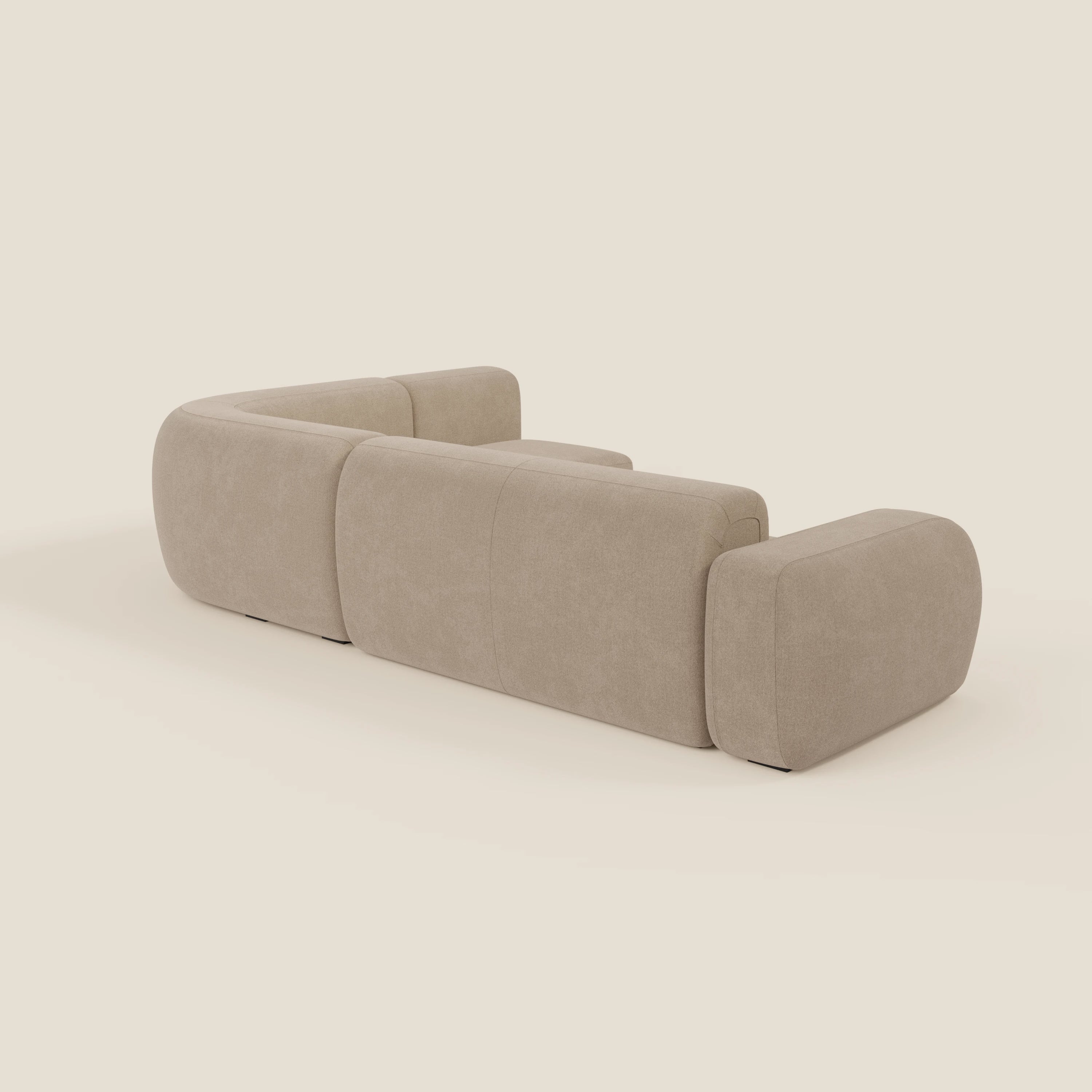 Il divano angolare componibile e modulare BonBon di Divani.Store, presentato in tessuto smacchiabile T23 beige, è caratterizzato da tre ampie sezioni arrotondate con imbottitura in peluche e braccioli a basso profilo, visti dallo schienale su sfondo crema.