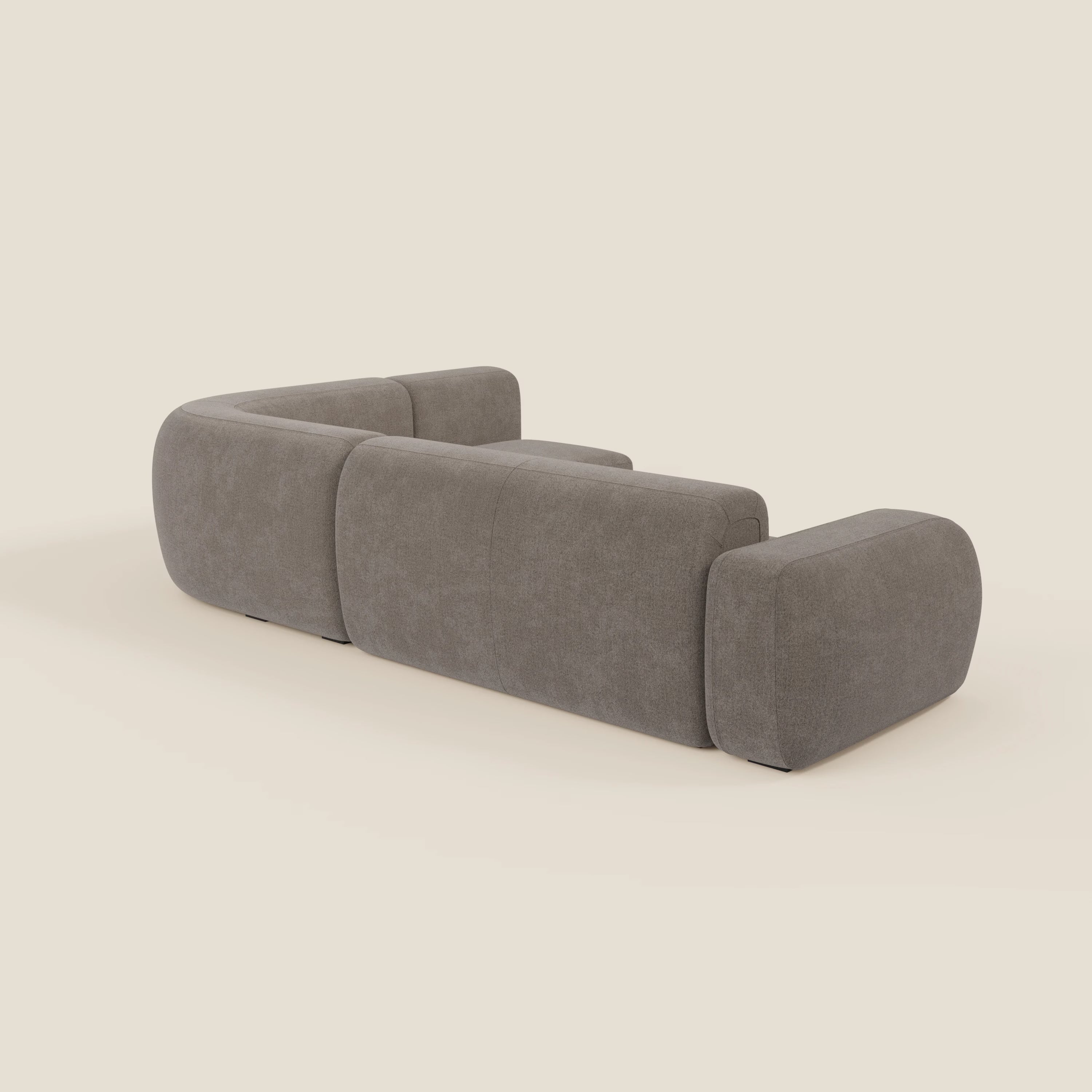 Il divano angolare componibile e modulare BonBon di Divani.Store in tessuto smacchiabile T23 talpa è caratterizzato da un design moderno e minimalista con bordi arrotondati e cuscini in tessuto felpato, mostrato dal retro su uno sfondo beige chiaro. Non sono visibili gambe o decori.