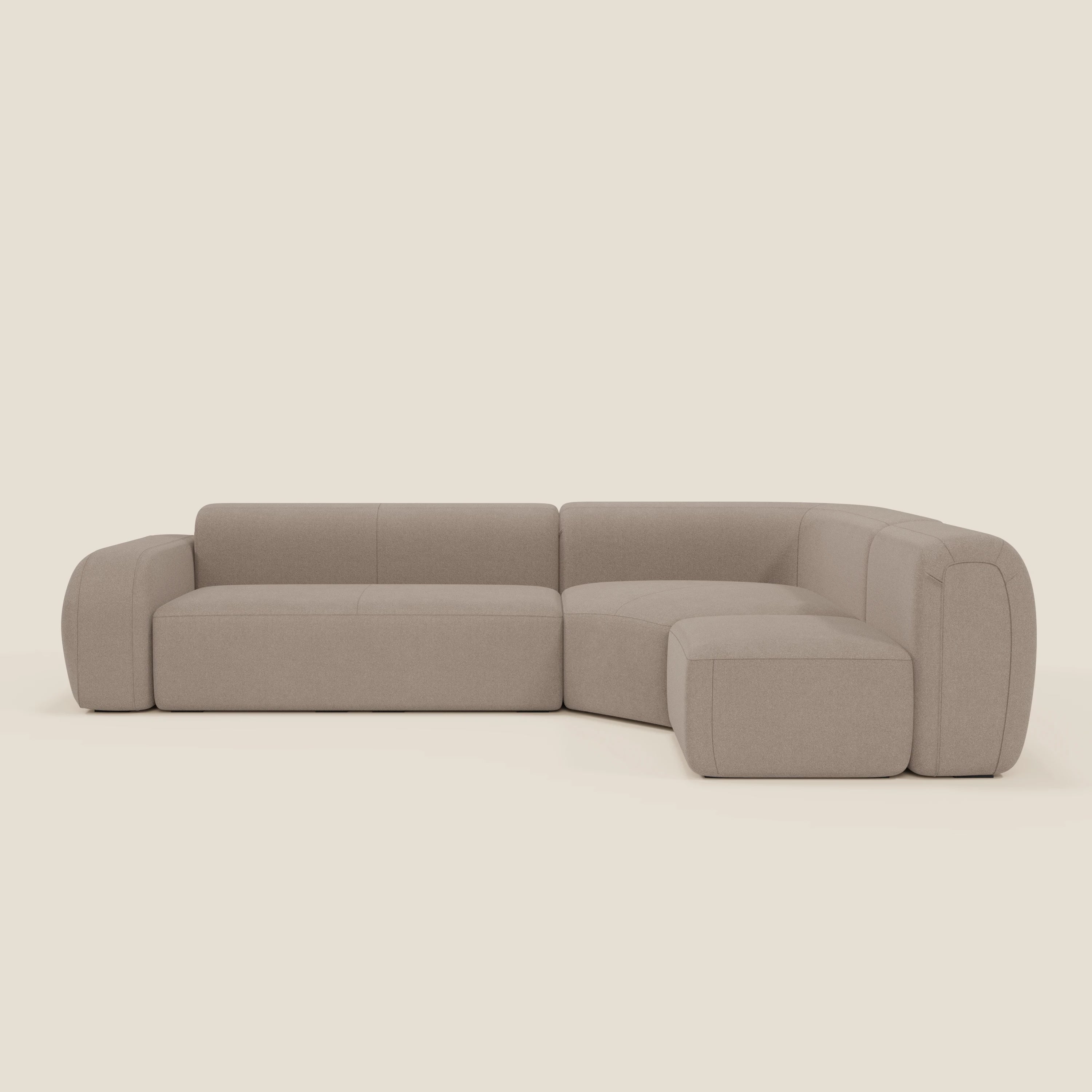 Il divano BonBon angolare componibile e modulare di Divani.Store è caratterizzato da cuscini e braccioli spessi e arrotondati in tessuto smacchiabile T23 tortora, con un design minimal dalle linee morbide su sfondo bianco sporco.