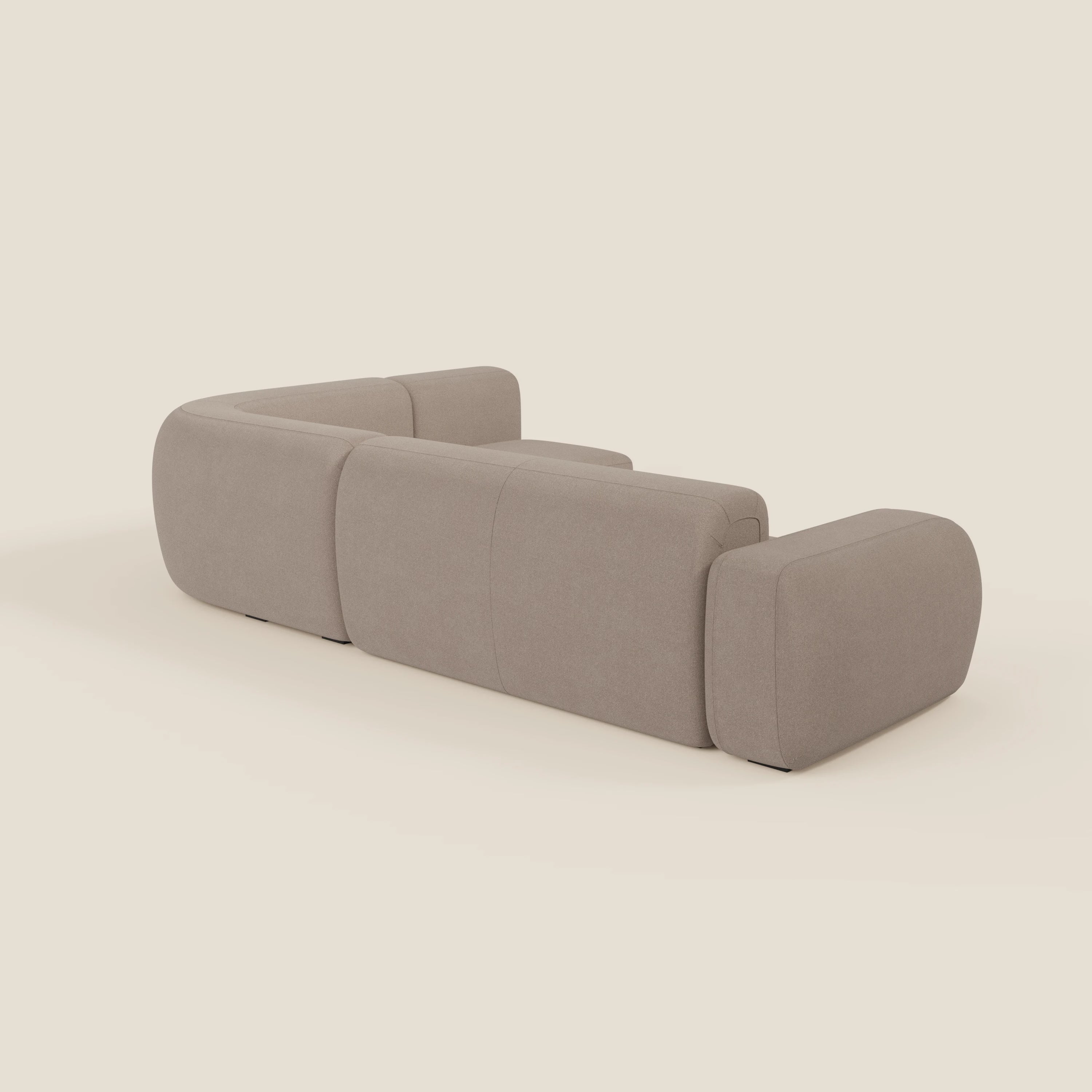 Il divano BonBon angolare componibile e modulare di Divani.Store in smacchiabile T23 tortora è caratterizzato da bordi morbidi e curvi e da un design minimalista con braccioli e schienali arrotondati, visti da un'angolazione laterale posteriore su uno sfondo semplice.