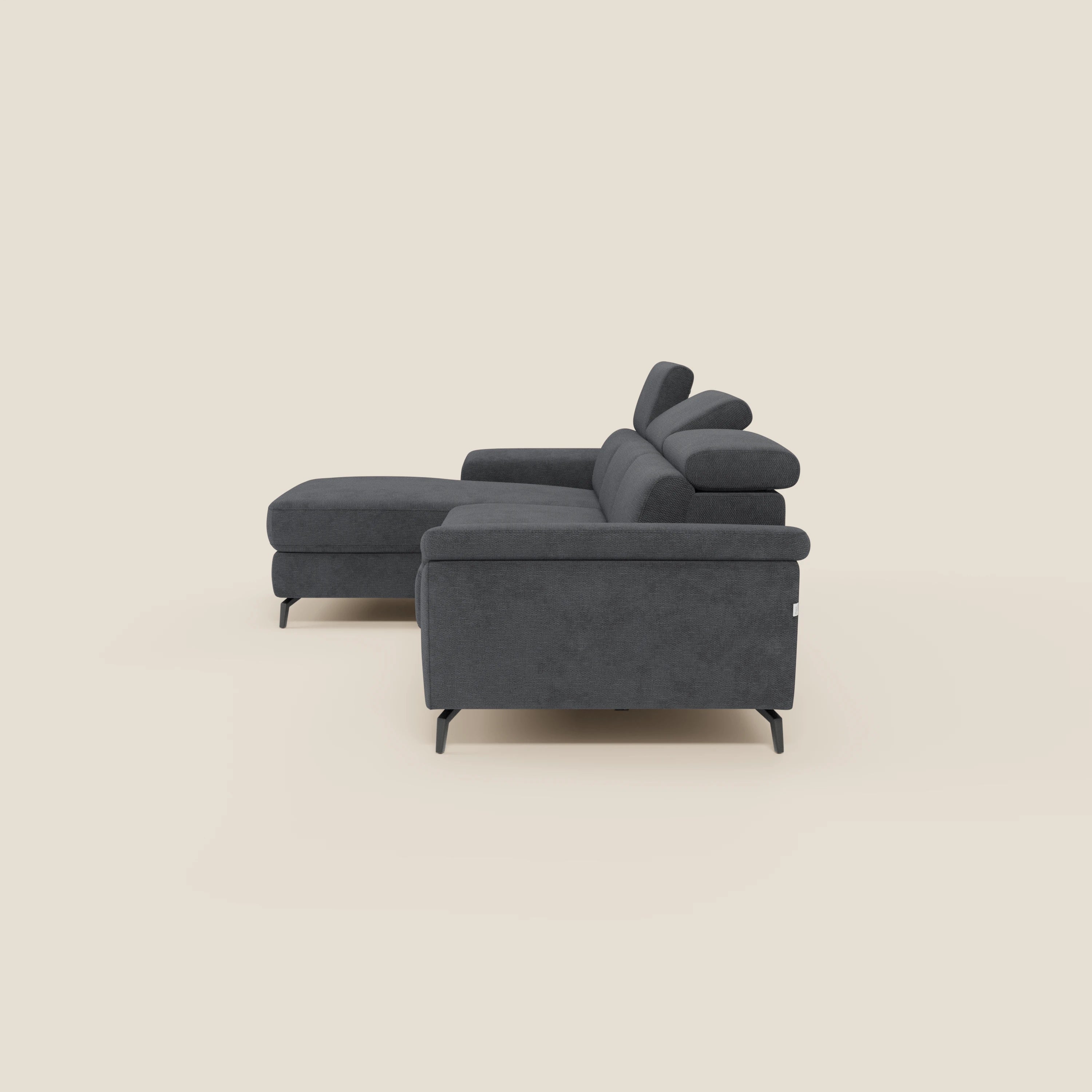 L'Estro Divano estraibile con chaise-longue e poggiatesta reclinabili T14 antracite di Divani.Store è presentato lateralmente su uno sfondo beige chiaro, che mette in risalto il suo design moderno e la chaise-longue sul lato sinistro.