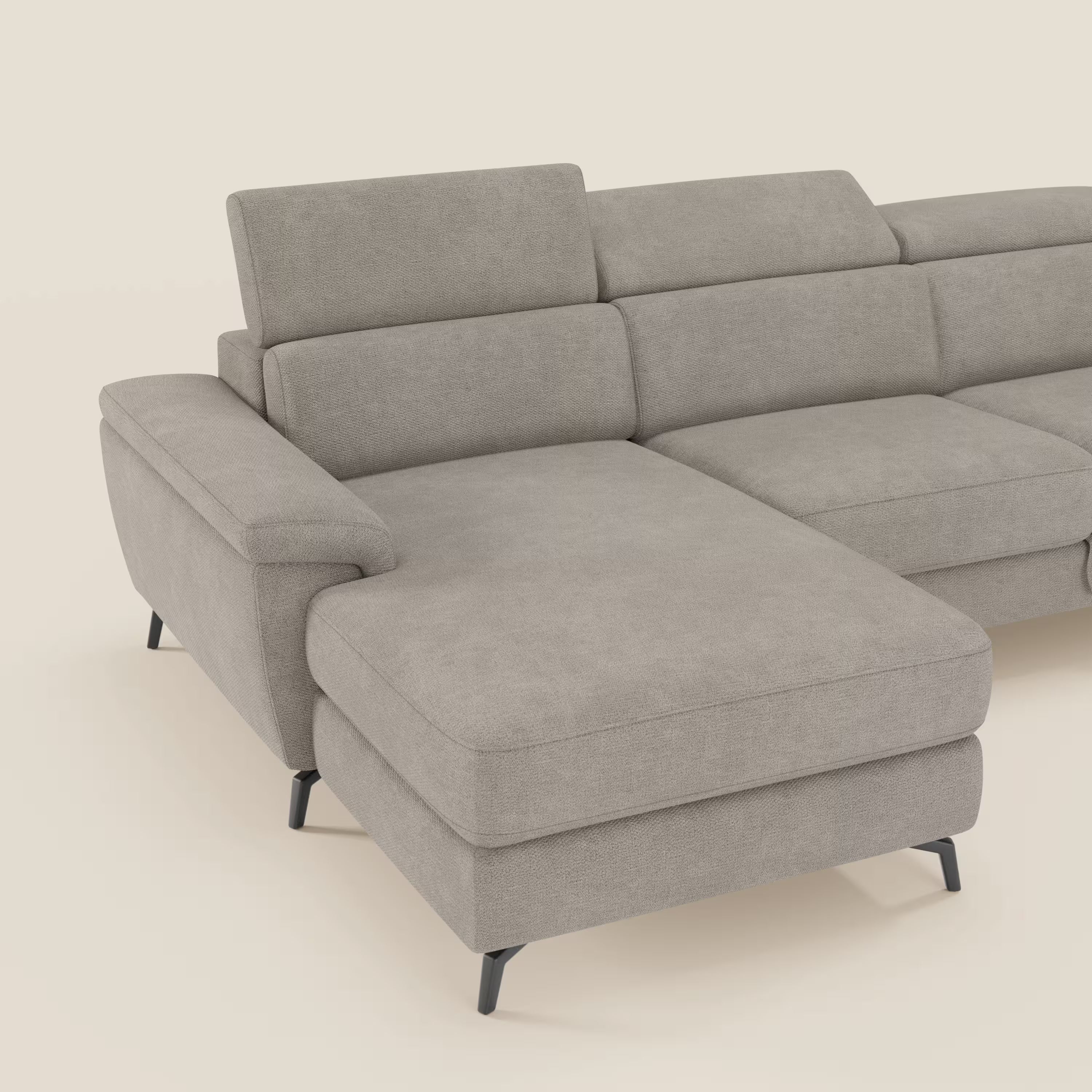 Il divano estraibile Estro di Divani.Store è un divano a L con chaise-longue a sinistra, poggiatesta reclinabile, tessuto tortora T14 impermeabile, ampi cuscini e sottili gambe in metallo nero su sfondo bianco sporco.