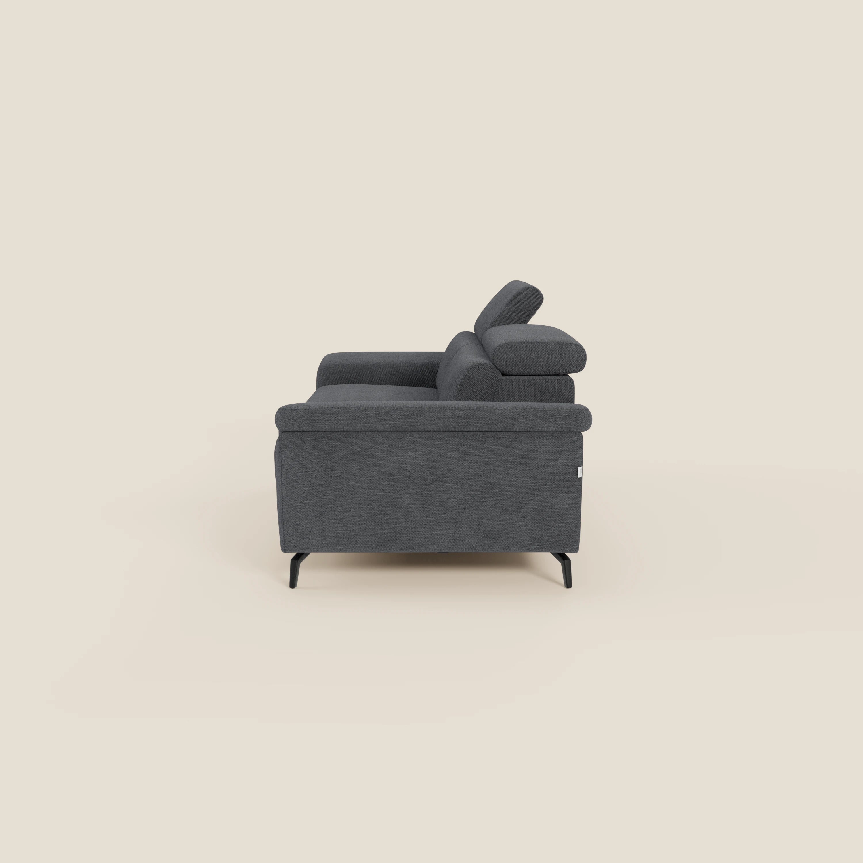 Estro Divano 3 posti con pouf estraibile di Divani.Store, in tessuto impermeabile T14 antracite, è caratterizzato da braccioli imbottiti, poggiatesta reclinabili e gambe corte angolate nere. Vista laterale su sfondo beige chiaro.