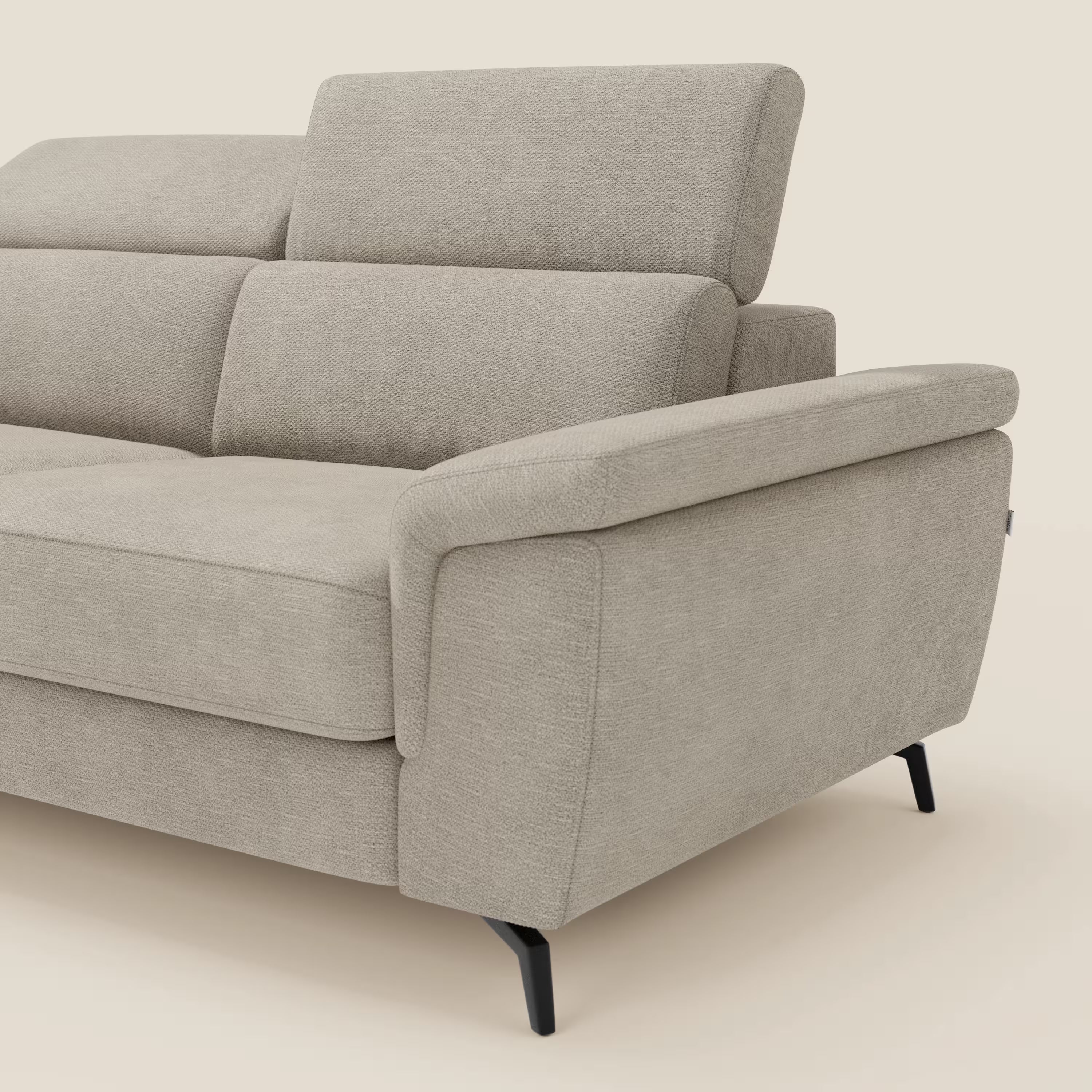 Primo piano di Estro Divano 3 posti con pouf estraibile di Divani.Store in beige impermeabile T14, con poggiatesta reclinabili, morbidi cuscini, ampi braccioli imbottiti e sottili gambe in metallo nero su sfondo chiaro.