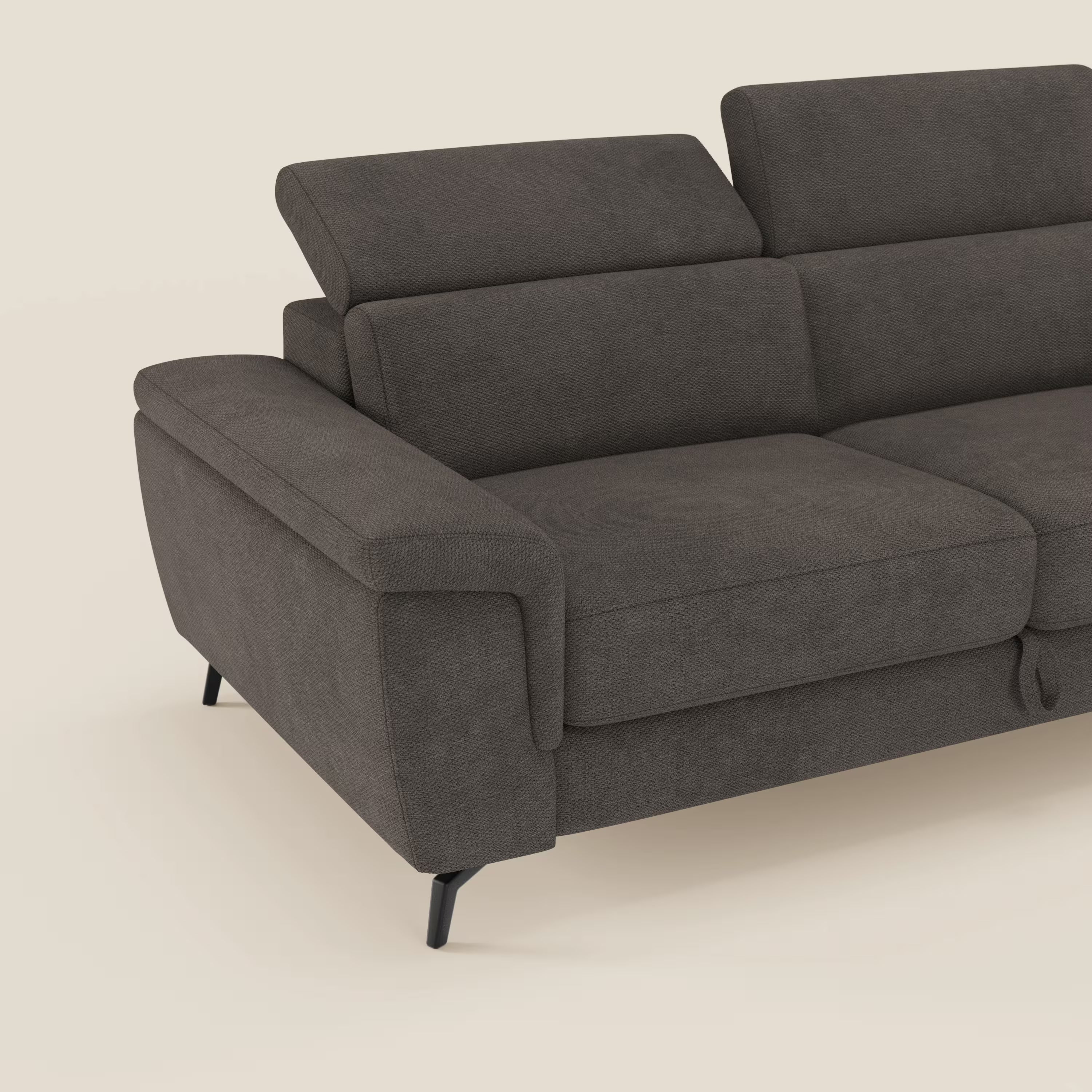 Un primo piano di Estro Divano 3 posti con pouf estraibile di Divani.Store in impermeabile T14 marrone mostra gli ampi braccioli, i due poggiatesta reclinabili e le gambe angolate nere. Solo il lato sinistro è visibile su uno sfondo beige chiaro.