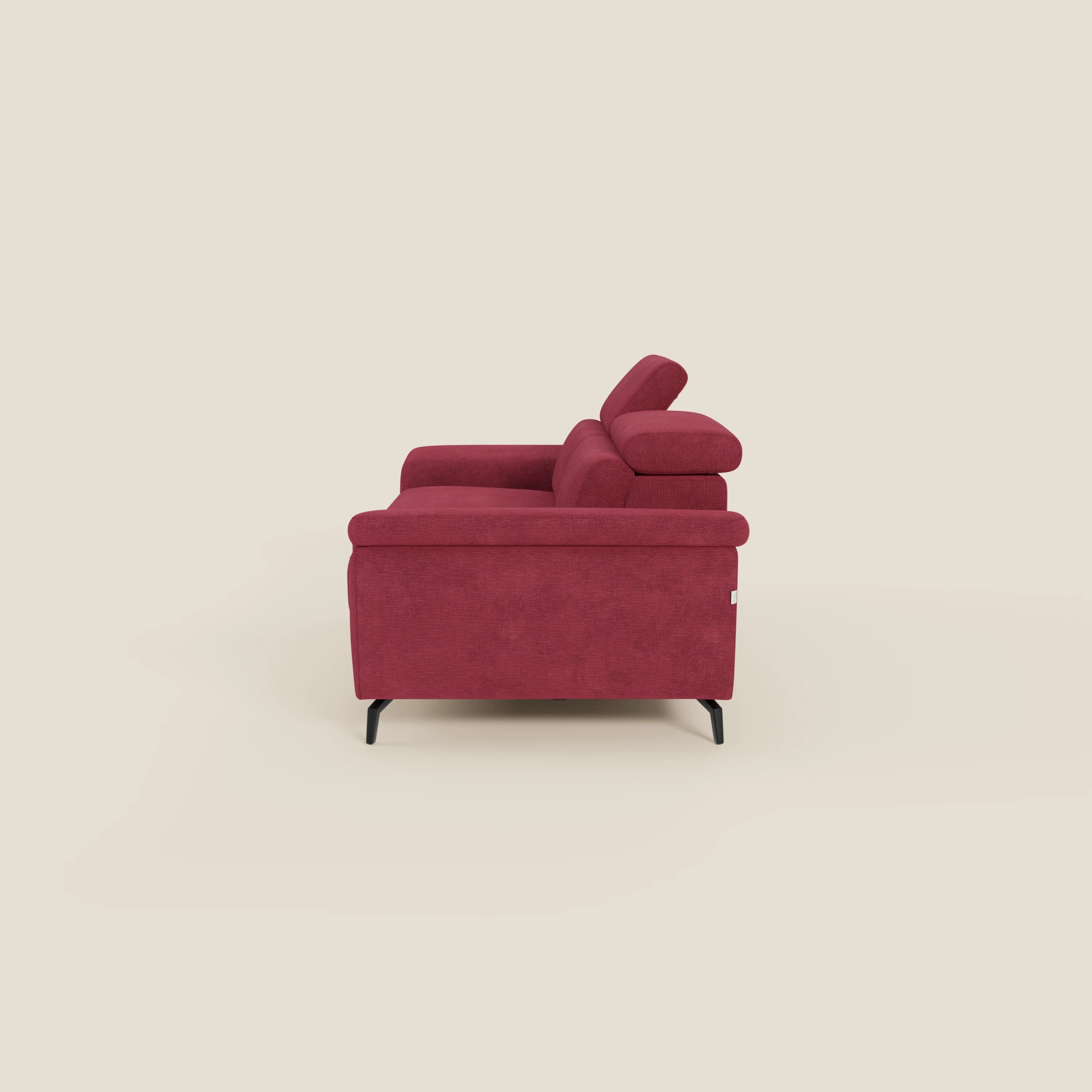 L'Estro Divano 3 posti con pouf estraibile di Divani.Store in impermeabile T14 rosso è caratterizzato da poggiatesta regolabili, cuscini in peluche, ampi braccioli e sottili gambe nere, mostrate di lato su uno sfondo beige.