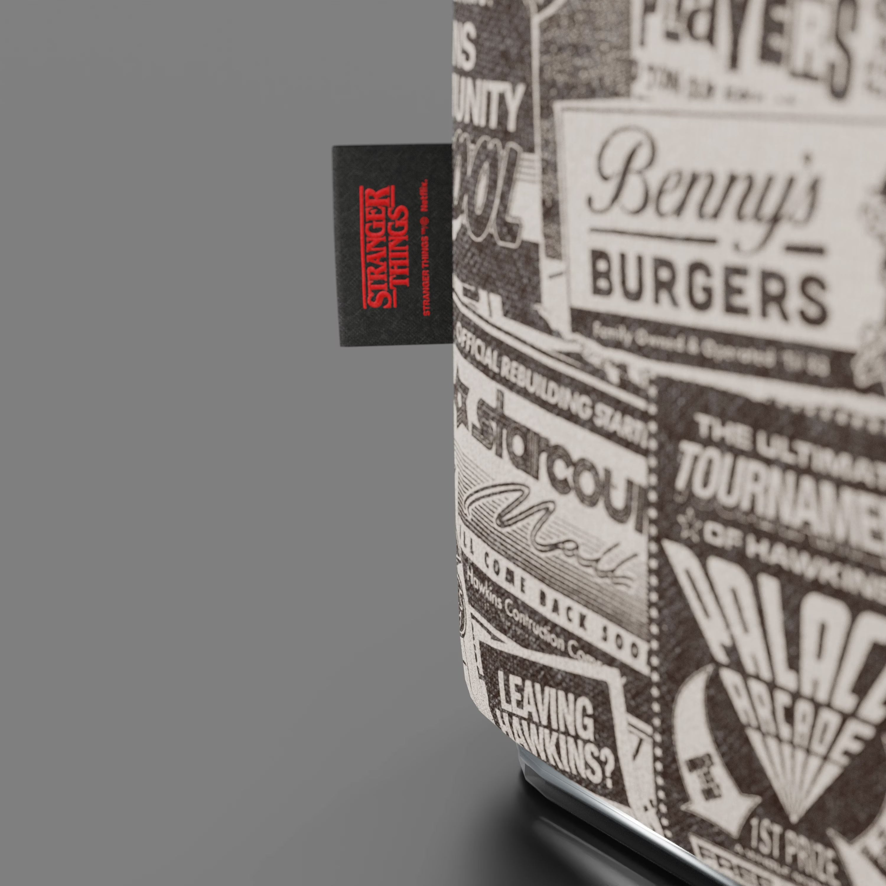 Primo piano del Pouf Cube Hawkins Post Stranger Things - Limited Edition Netflix di Divani.Store, caratterizzato da pubblicità vintage in bianco e nero come "Benny's Burgers" e da un'etichetta Limited Edition cucita. Ideale per ogni fan di Stranger Things o per un arredamento di stile. Sfondo grigio.