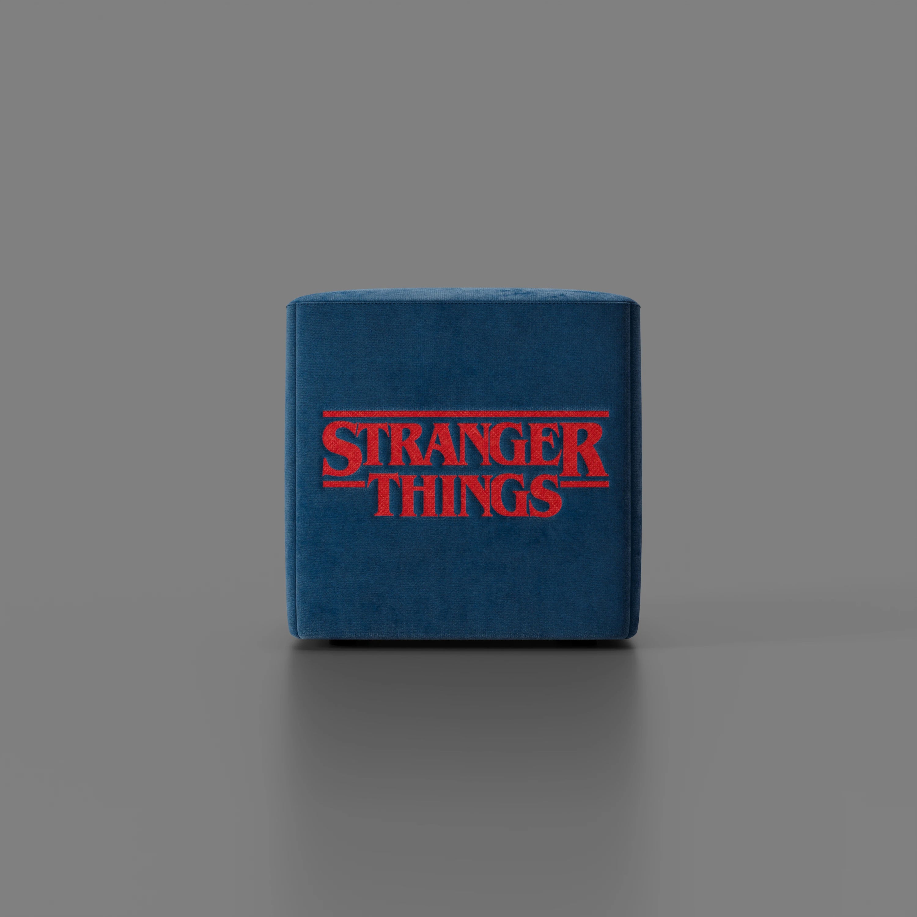 Il pouf Cube Stranger Things Edition di Divani.Store è caratterizzato da un logo rosso in grassetto su tessuto blu resistente alle sbavature, esposto su una superficie grigia che mette in risalto il suo design unico della cultura pop.