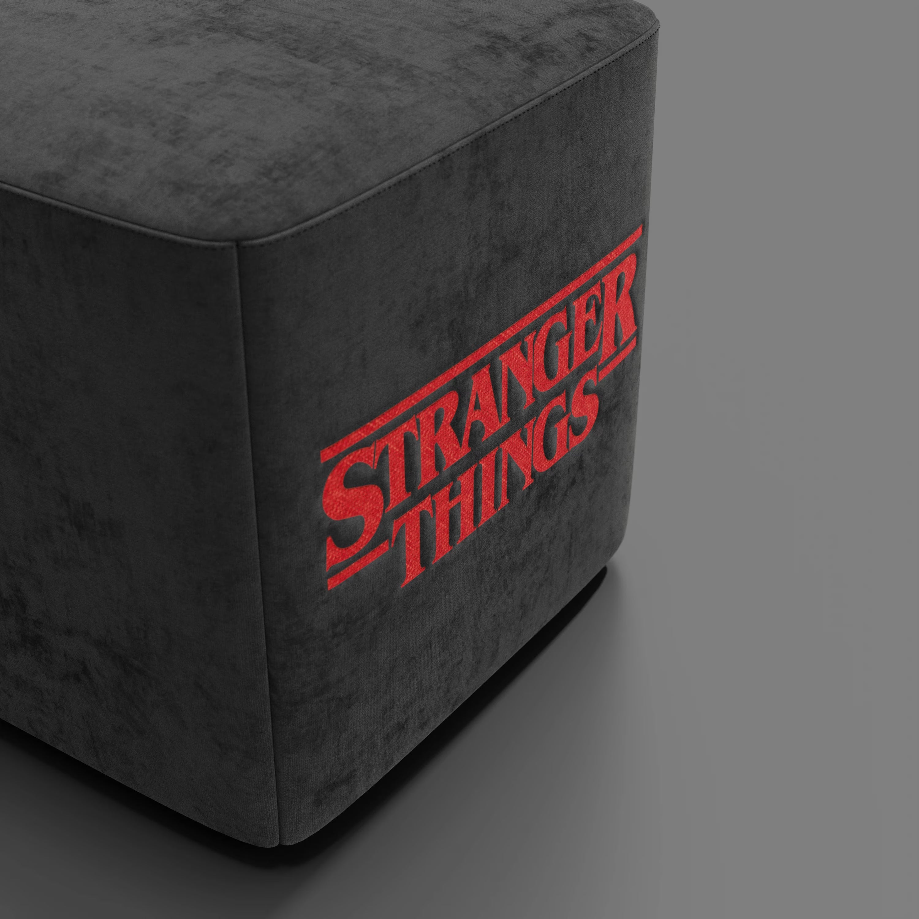 Il pouf Cube Stranger Things Edition di Divani.Store è caratterizzato da un tessuto antracite antimacchia con l'iconico logo rosso della serie ricamato su un lato, che unisce la morbida texture del velluto e il design retrò in una silhouette pulita e moderna.