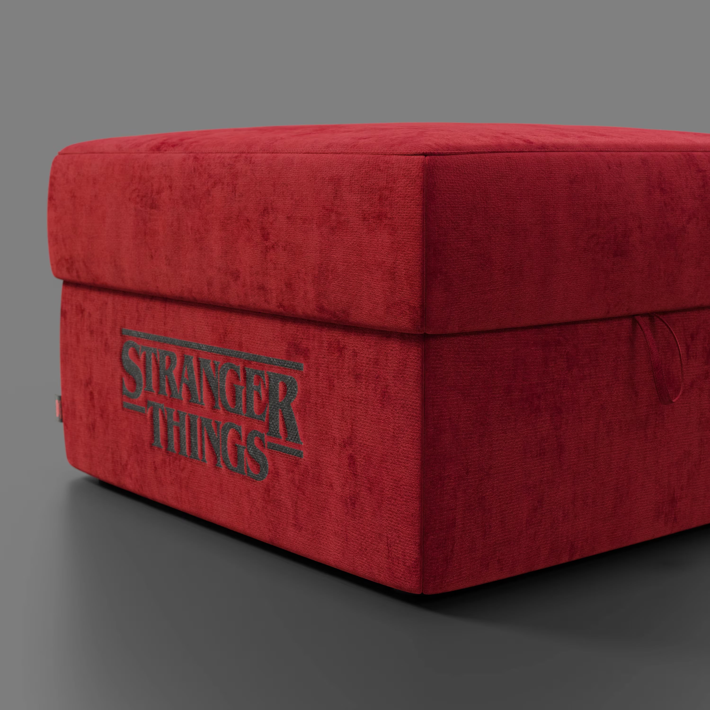 Un pouf rosso Sun Contenitore Stranger Things Edition (60x80 cm) in tessuto antimacchia di Divani.Store, con il logo della serie, si trova su uno sfondo grigio: un pezzo d'arredamento in edizione speciale per i fan.