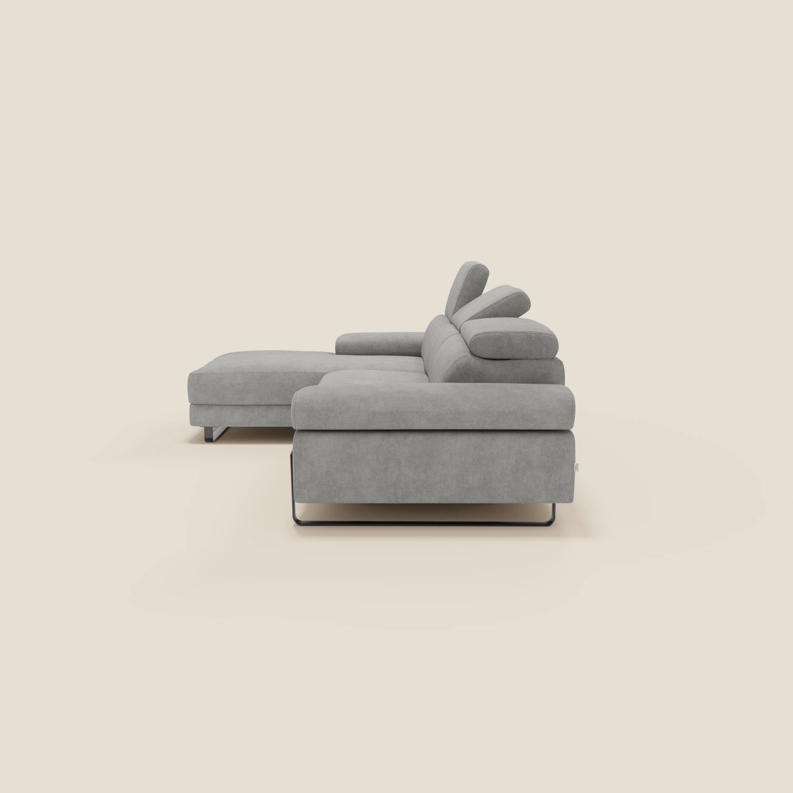 Il divano angolare estraibile Zayana di Divani.Store, in T02 grigio chiaro tessuto impermeabile, presenta una forma a L con braccioli e poggiatesta reclinabili, gambe basse in metallo e un look elegante su sfondo bianco sporco.