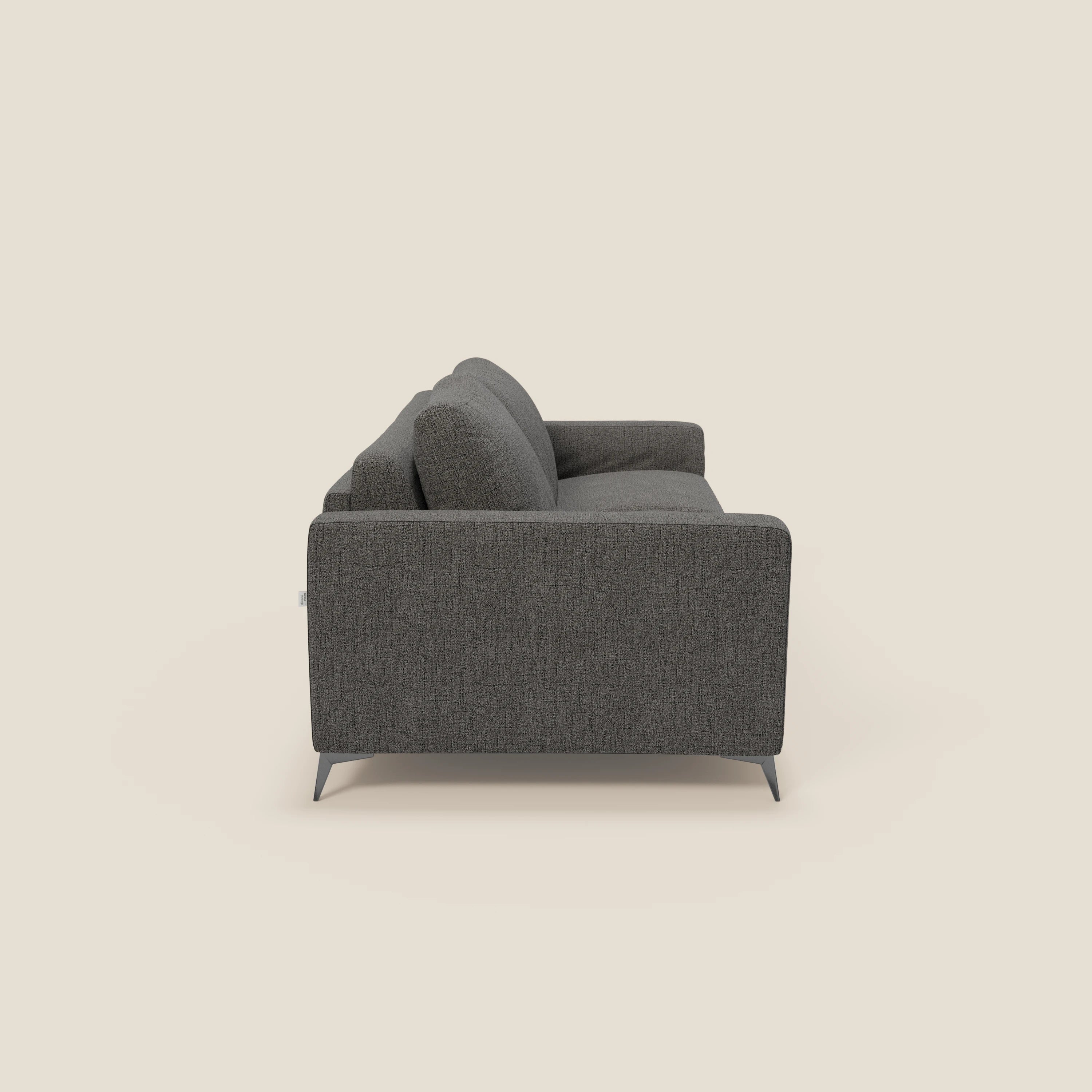 Vista laterale del divano letto matrimoniale Alaya di Divani.Store in tessuto impermeabile T03 antracite, con gambe angolari in metallo, spessi cuscini di seduta e di schienale e braccioli dritti, su sfondo beige chiaro.