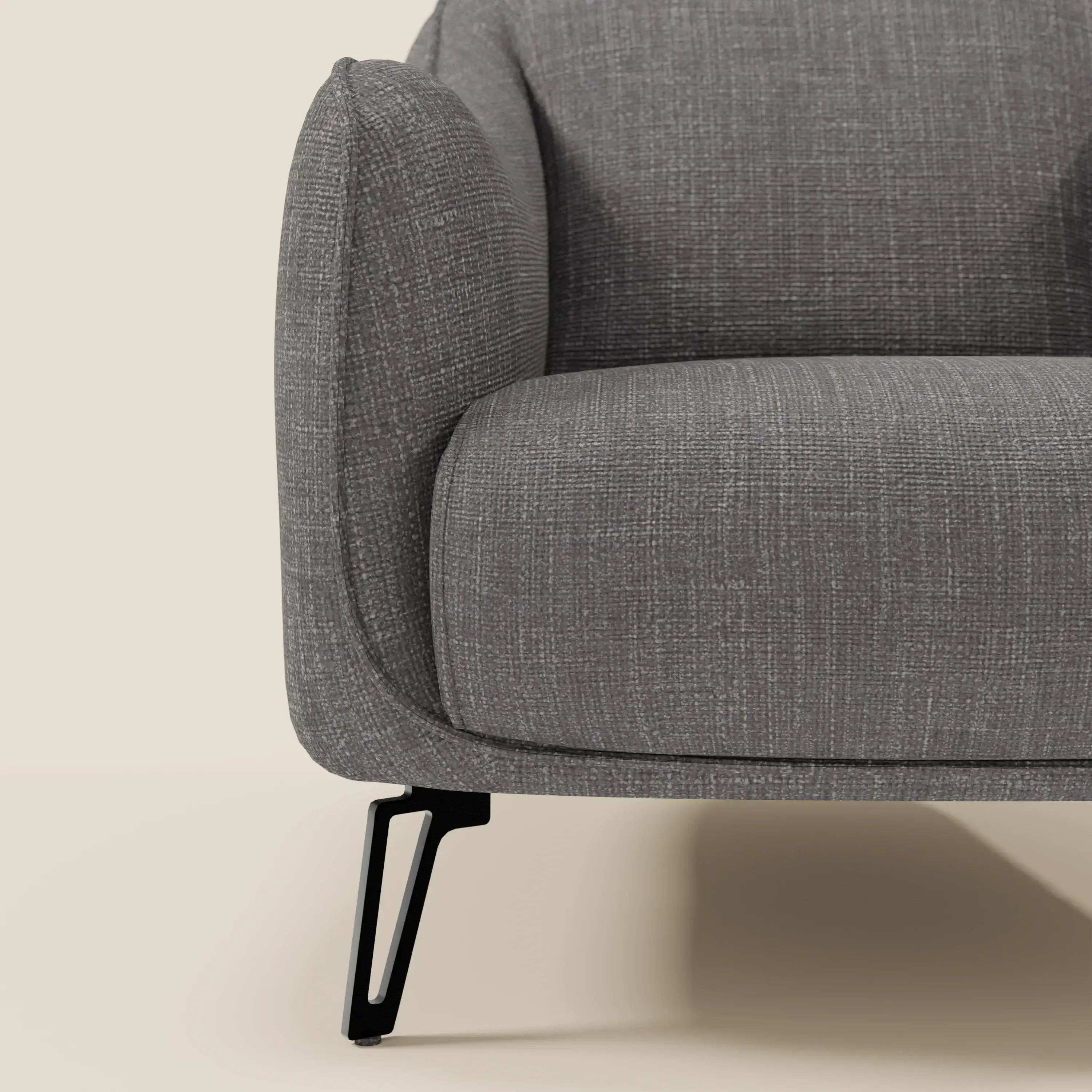 Primo piano di Avela Poltroncina di Divani.Store in morbido tessuto impermeabile T06 antracite. L'inquadratura mette in evidenza il bracciolo sinistro, il cuscino di seduta e la gamba in metallo nero su uno sfondo beige per un look minimalista e contemporaneo.