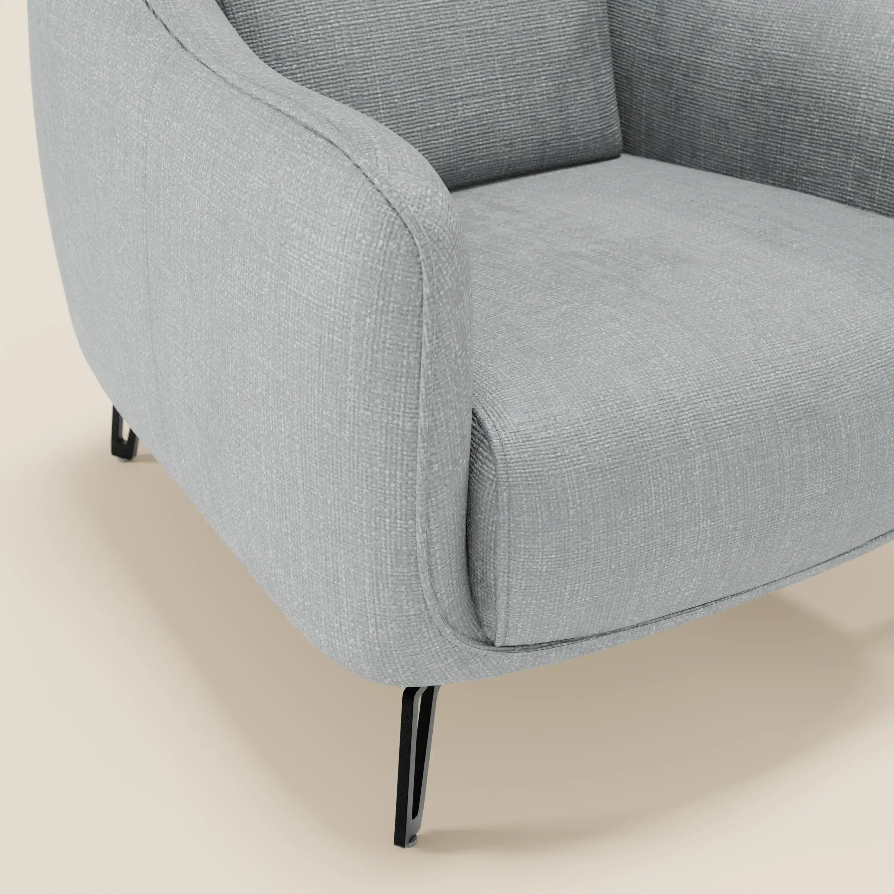 Primo piano di Avela Poltroncina di Divani.Store, caratterizzata da un comfort senza tempo in morbido tessuto T06 ghiaccio, resistente all'acqua. Il suo design contemporaneo, con bordi curvi e sottili gambe in metallo nero, spicca su uno sfondo beige chiaro.