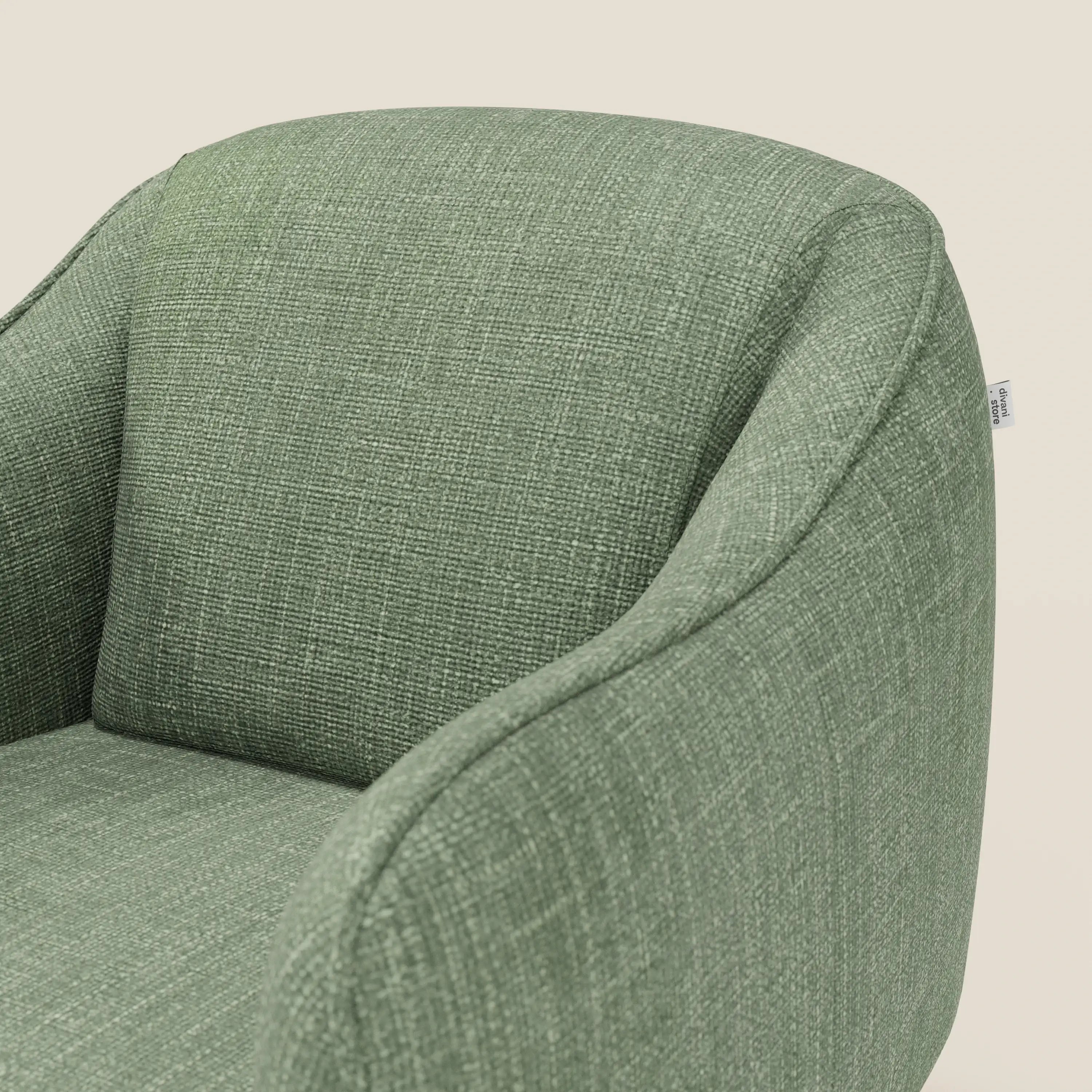 Primo piano di Avela Poltroncina di Divani.Store, in morbido tessuto impermeabile verde T06, con schienale curvo, braccioli arrotondati e una piccola targhetta laterale bianca, su sfondo beige chiaro.