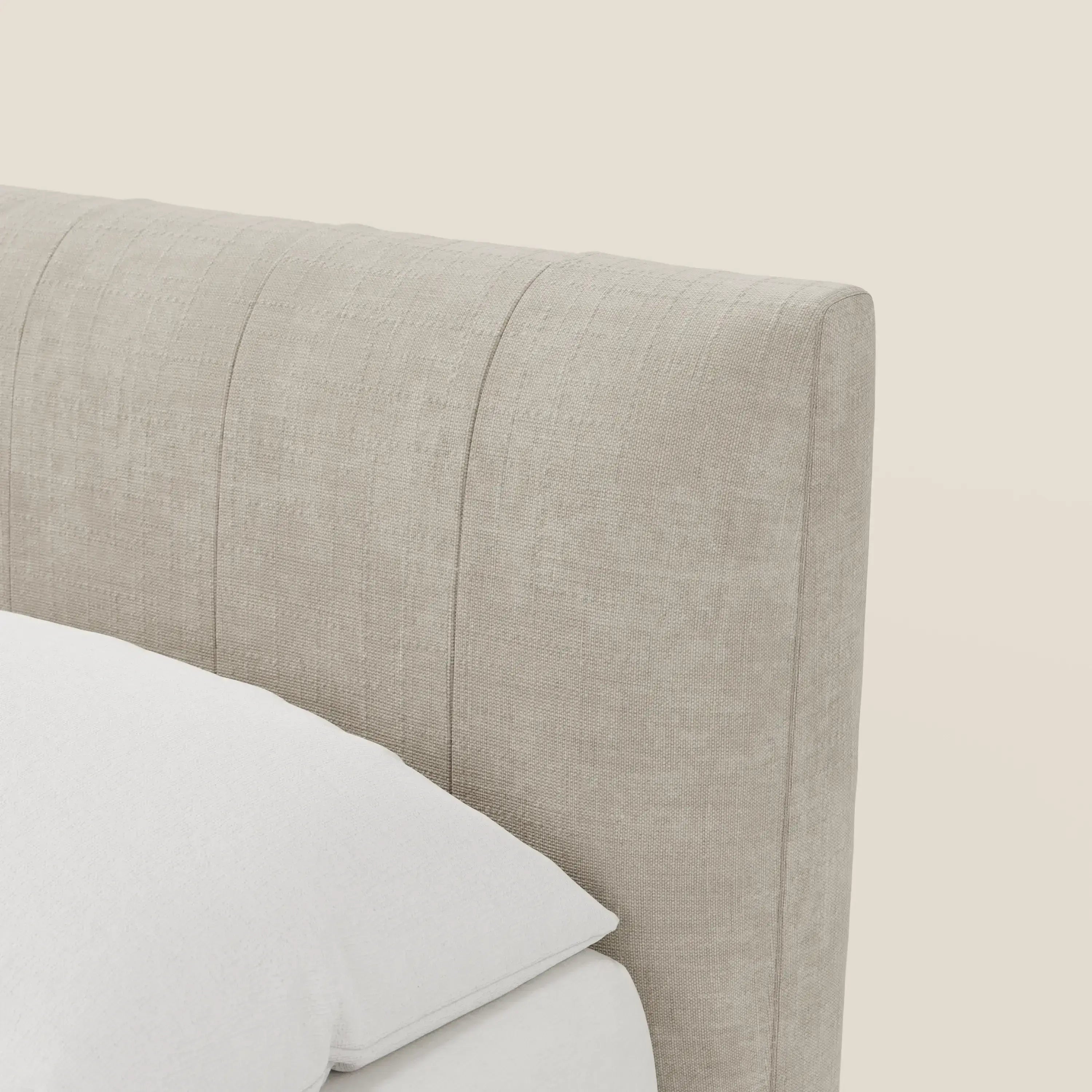Primo piano del letto contenitore Bogart beige Edizione Grande Fratello di Letti.store, con tessuto antimacchia T22 panna, sfoderabile e con cuciture verticali. Una parte del cuscino e del materasso bianchi appaiono su uno sfondo crema chiaro.