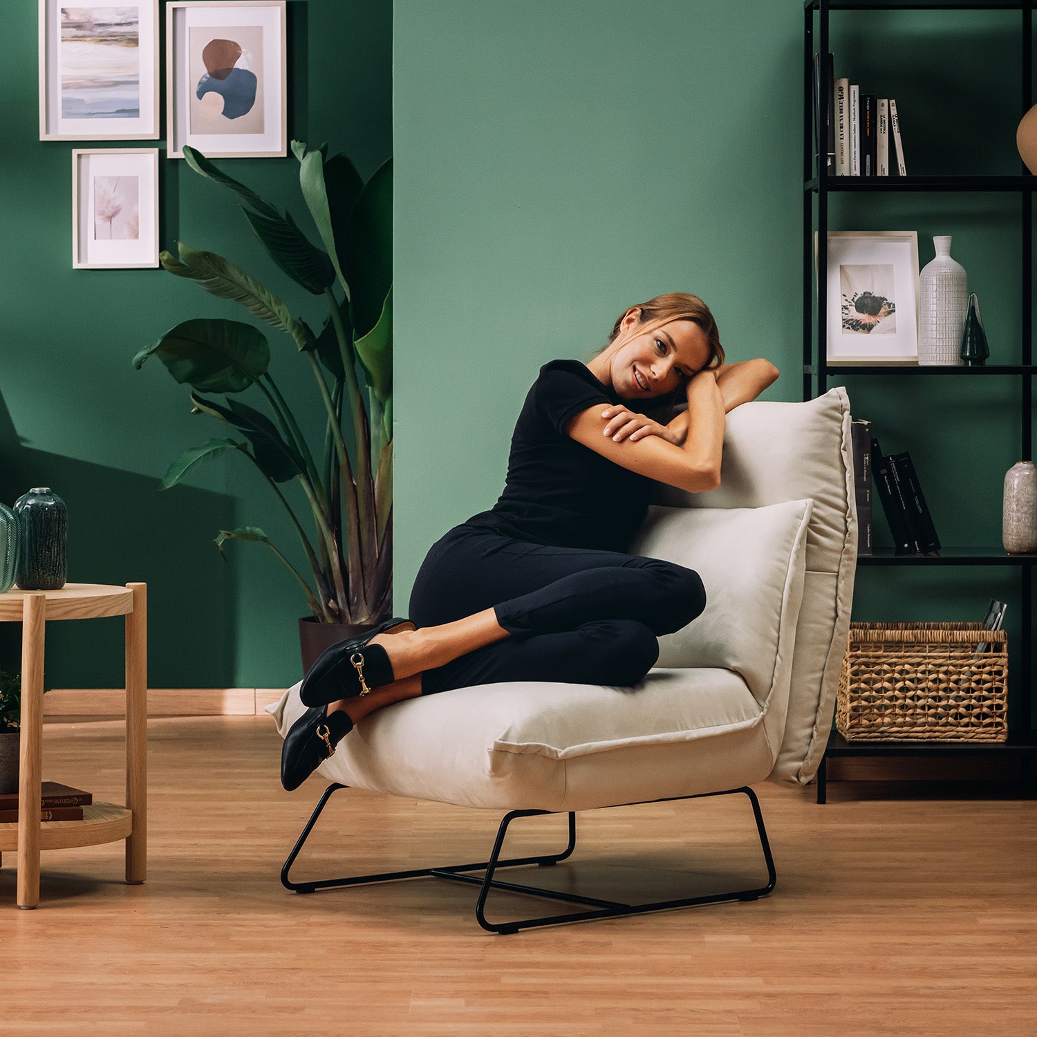 Una donna in nero si sdraia e sorride sulla Poltroncina Tessa dal design moderno in morbida microfibra smacchiabile T11 panna di Divani.Store, ambientata in un soggiorno moderno con pareti verdi e arredamento italiano di stile.